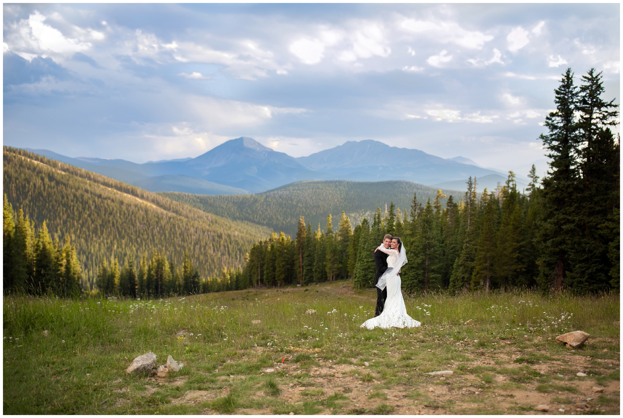 bride and groom hugging in a field with mountains in the background at Timber Ridge Keystone wedding