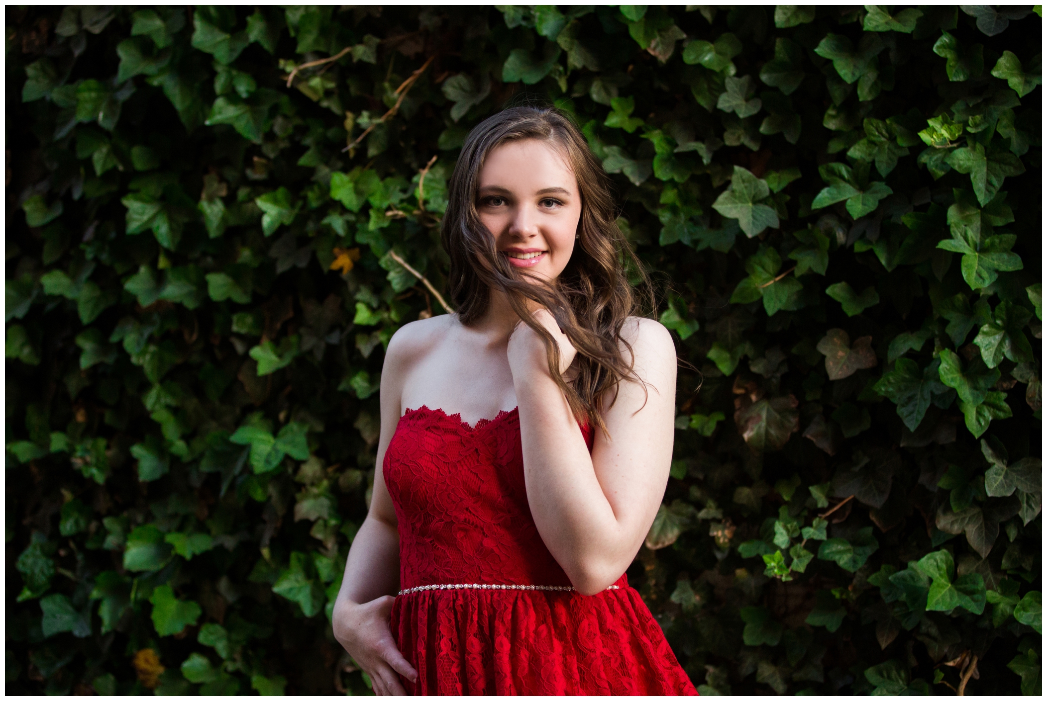 teen in red dress standing in front of ivy wall for Longmont Colorado senior portraits 