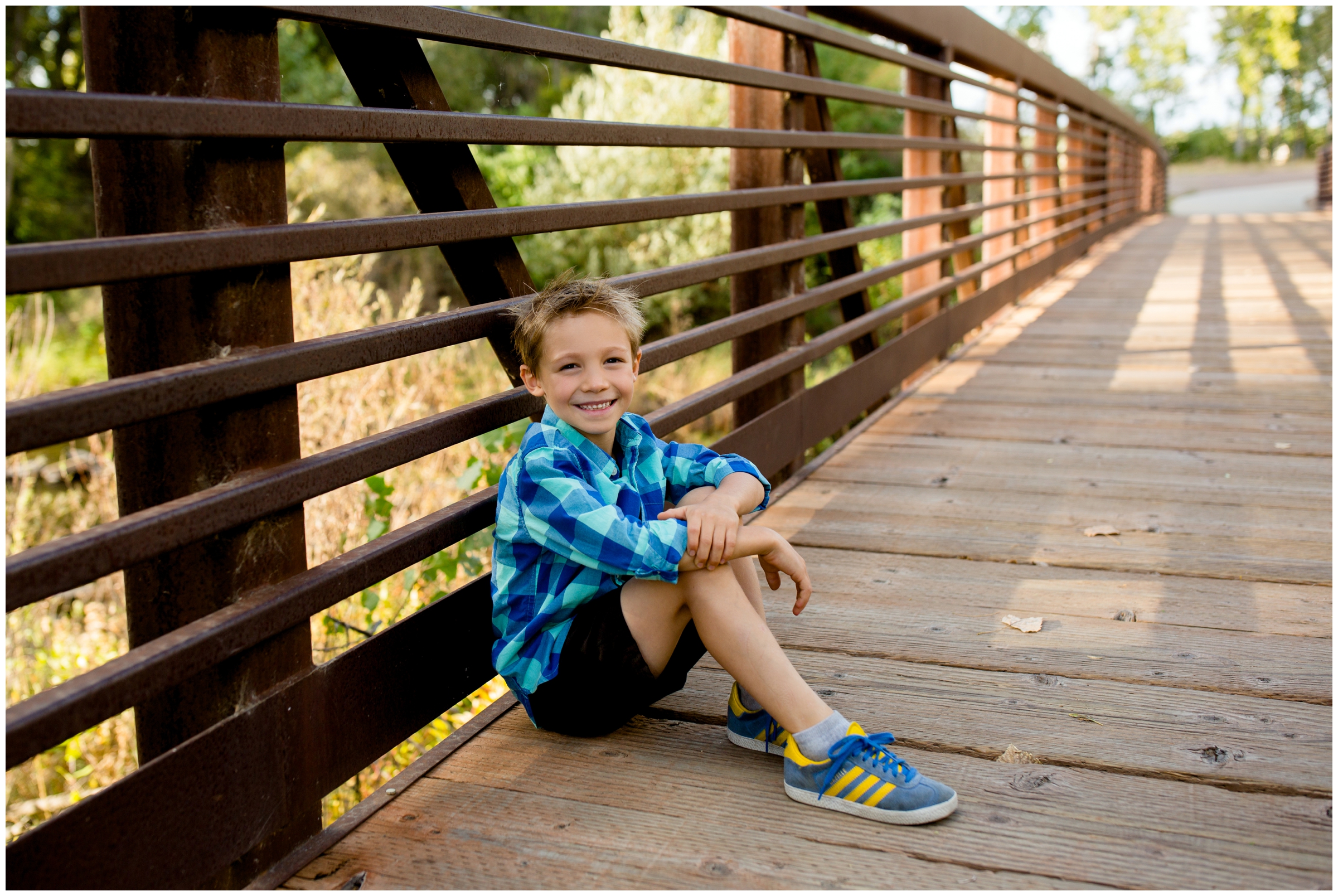 young boy sitting on bridge at Golden Ponds during Longmont Colorado family pictures in fall 