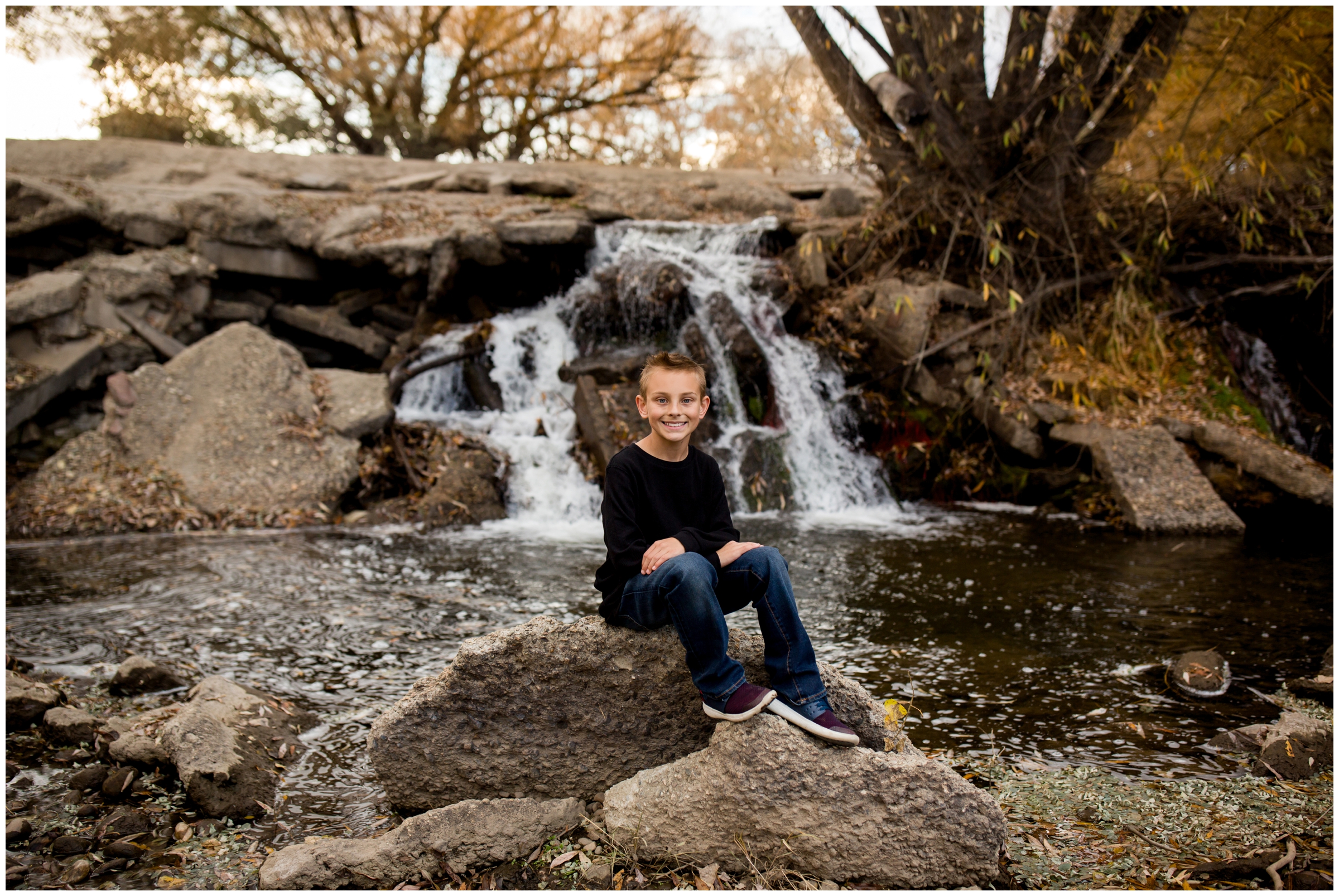 boy sitting on rock with waterfall in background at Golden Ponds Colorado 
