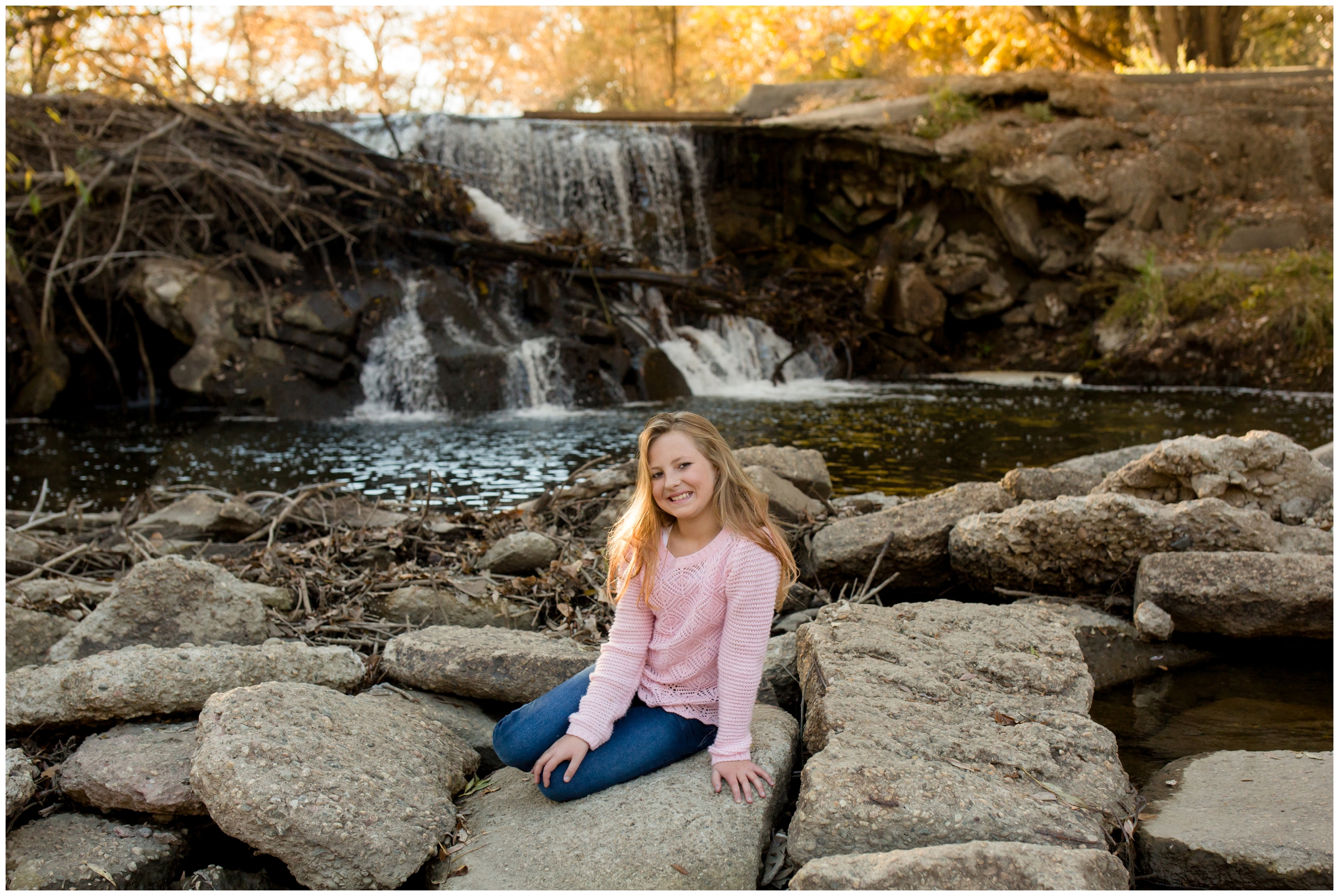 girl sitting on rocks with waterfall in background at Longmont family photography session 