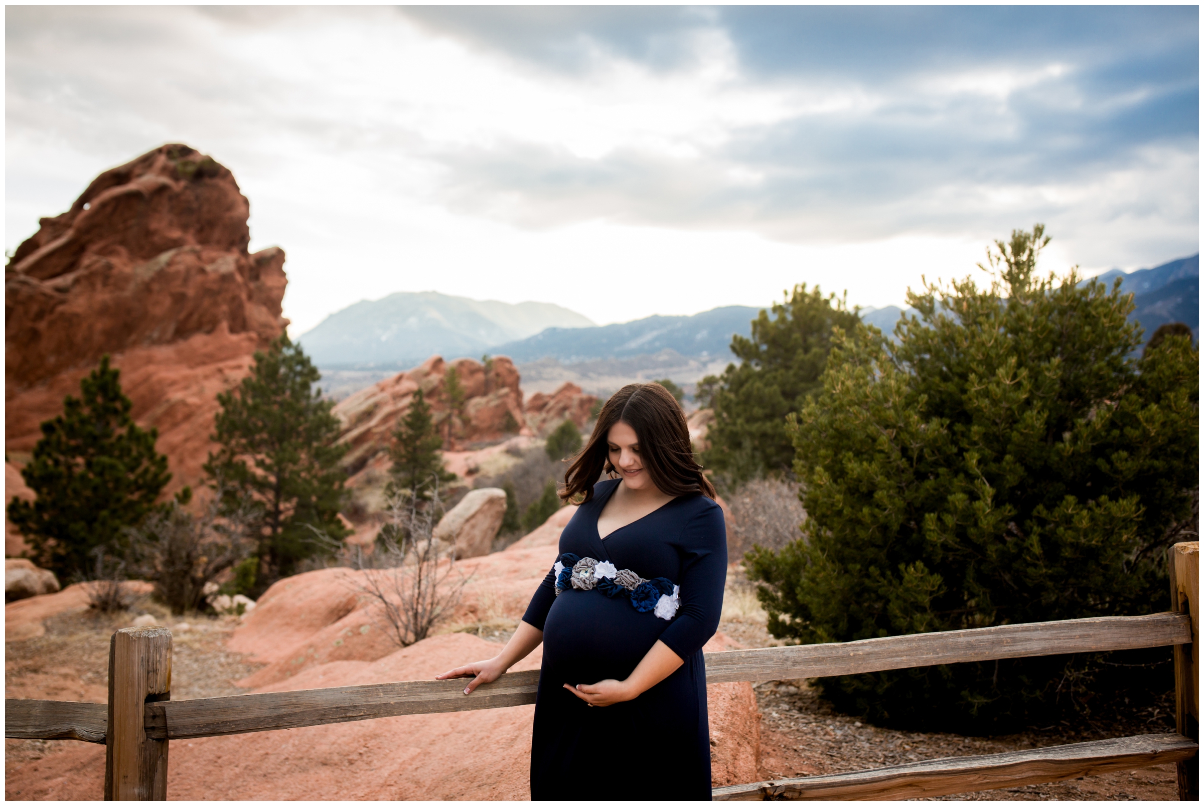 pregnant woman leaning on fence with garden of the gods in background at Colorado Springs maternity photos 