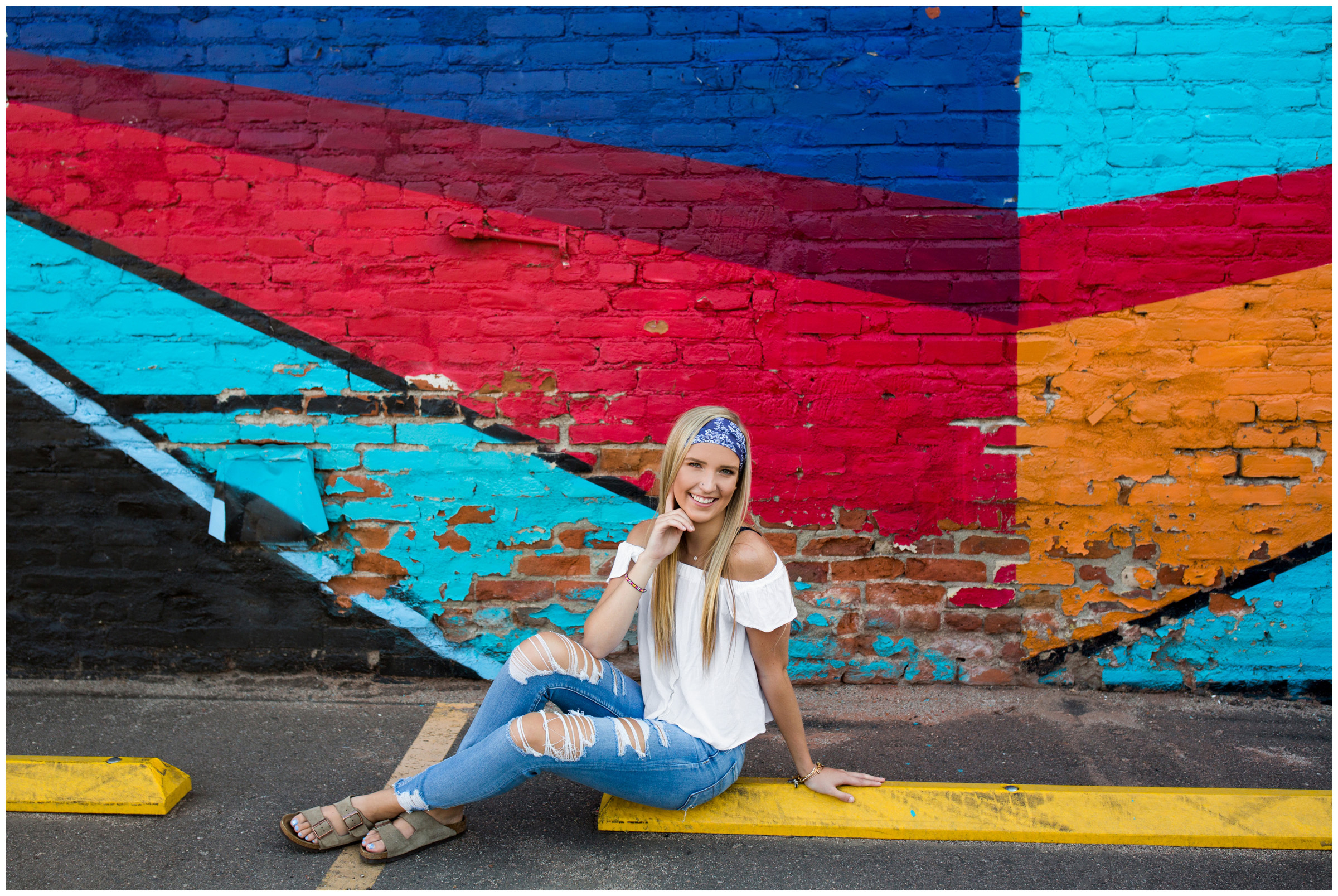 teen girl sitting on curb with art mural in background 
