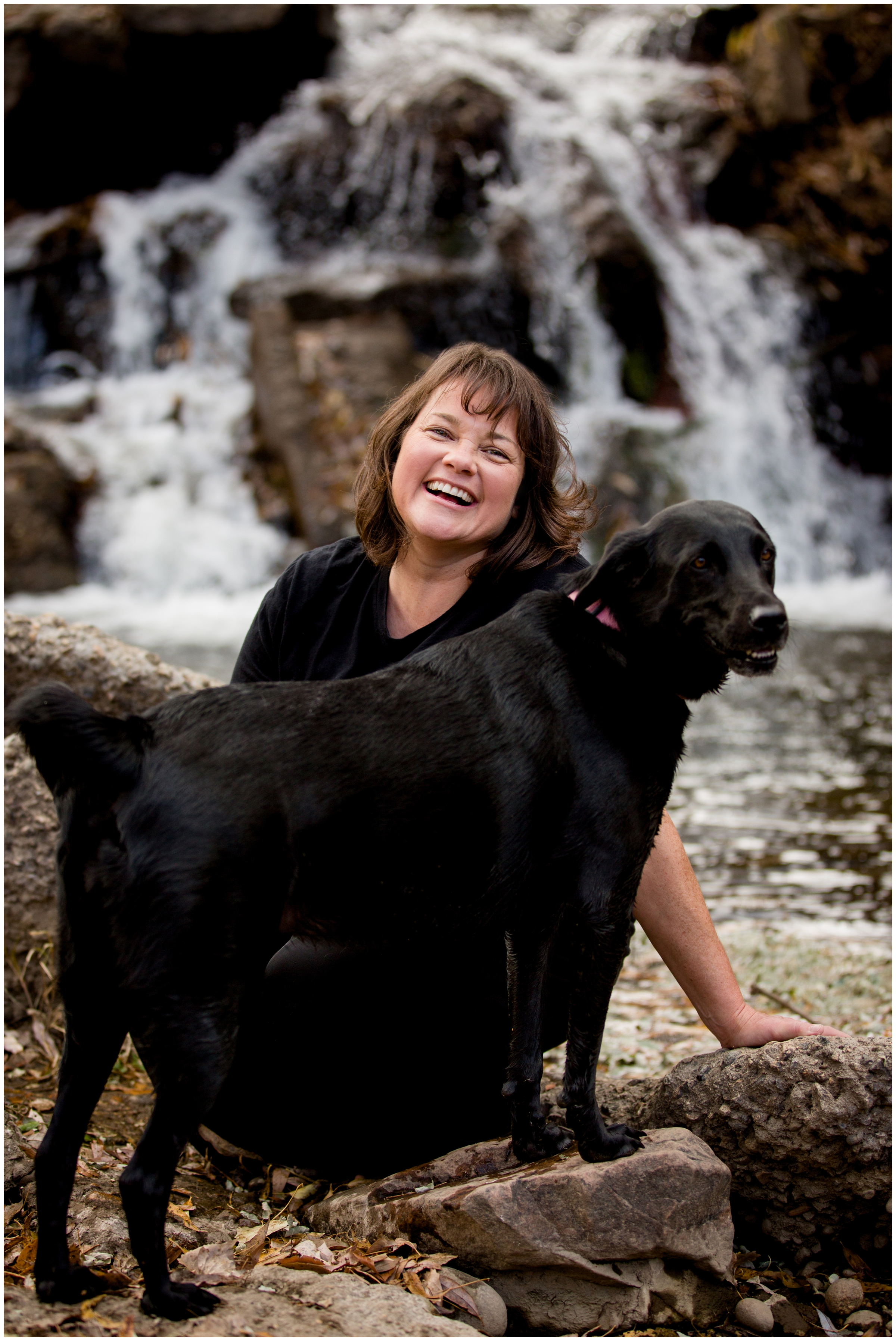 woman and her dog posing by a waterfall in Longmont Colorado at Golden Ponds family portraits 