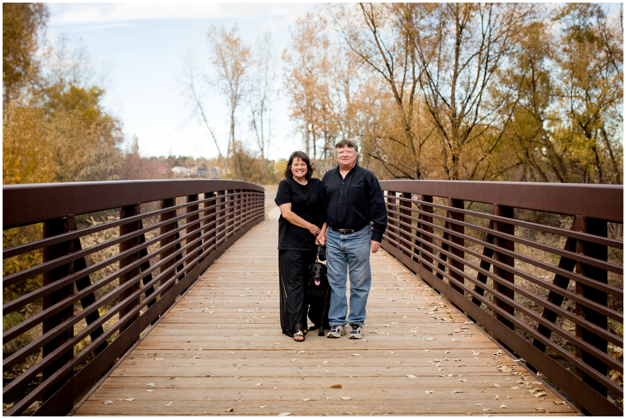 couple with their dog standing on wooden bridge 