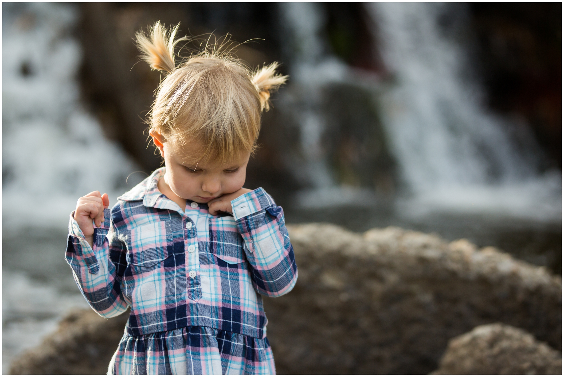 little girl with pigtails standing in front of waterfall 