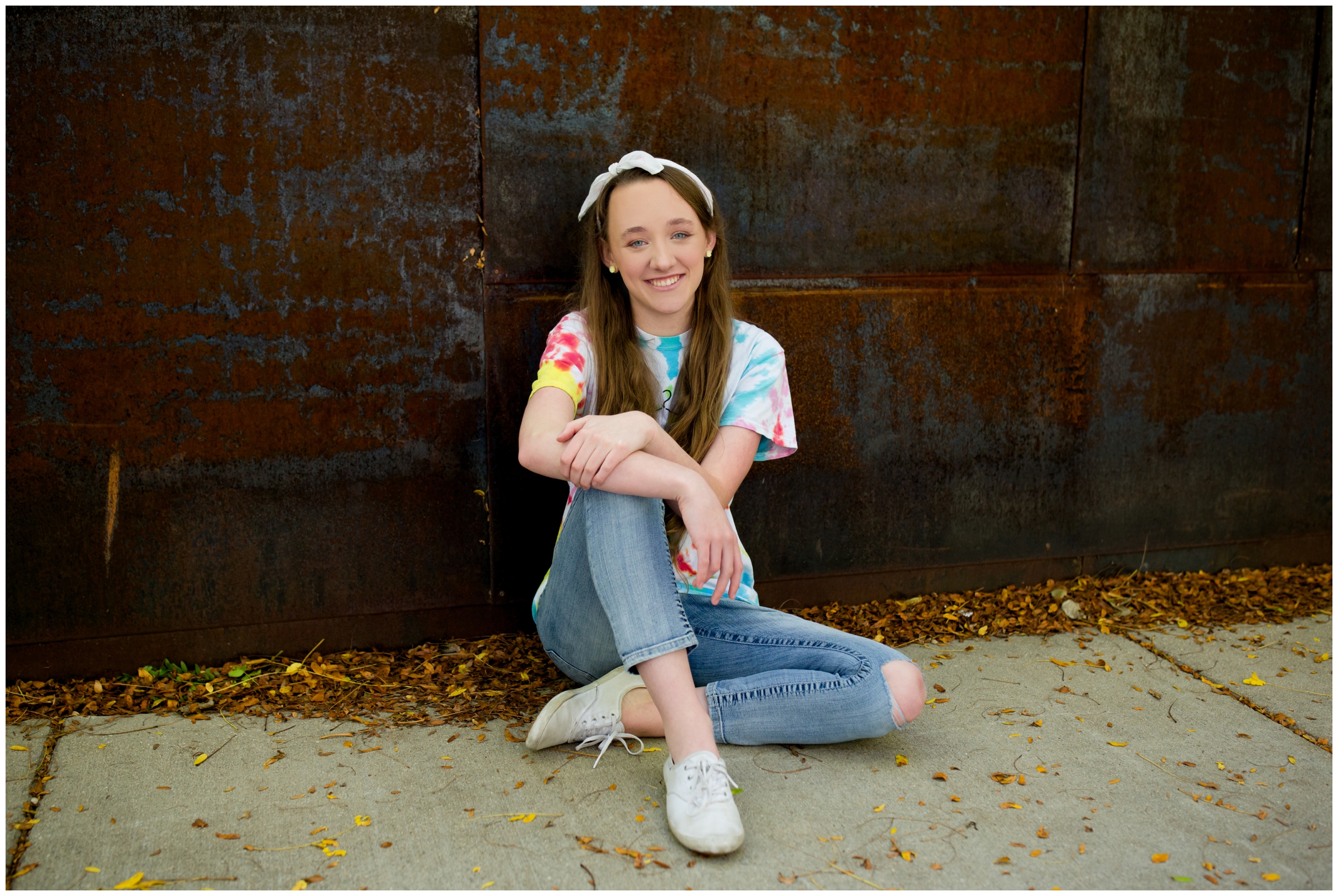 teen girl sitting against rust colored wall at Longmont Colorado senior pictures 