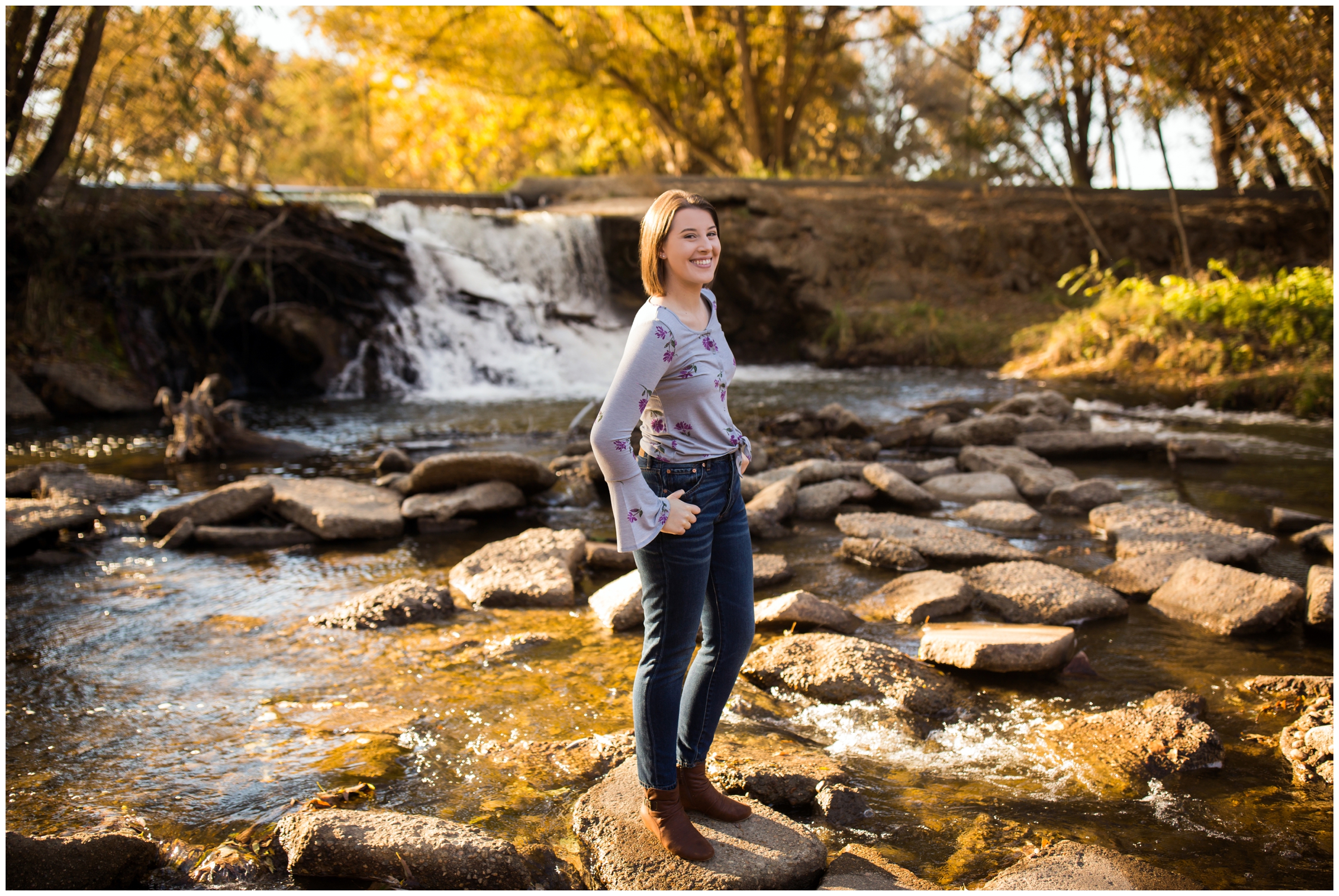Mead High School student posing with waterfall and fall foliage in background at Longmont senior portraits 