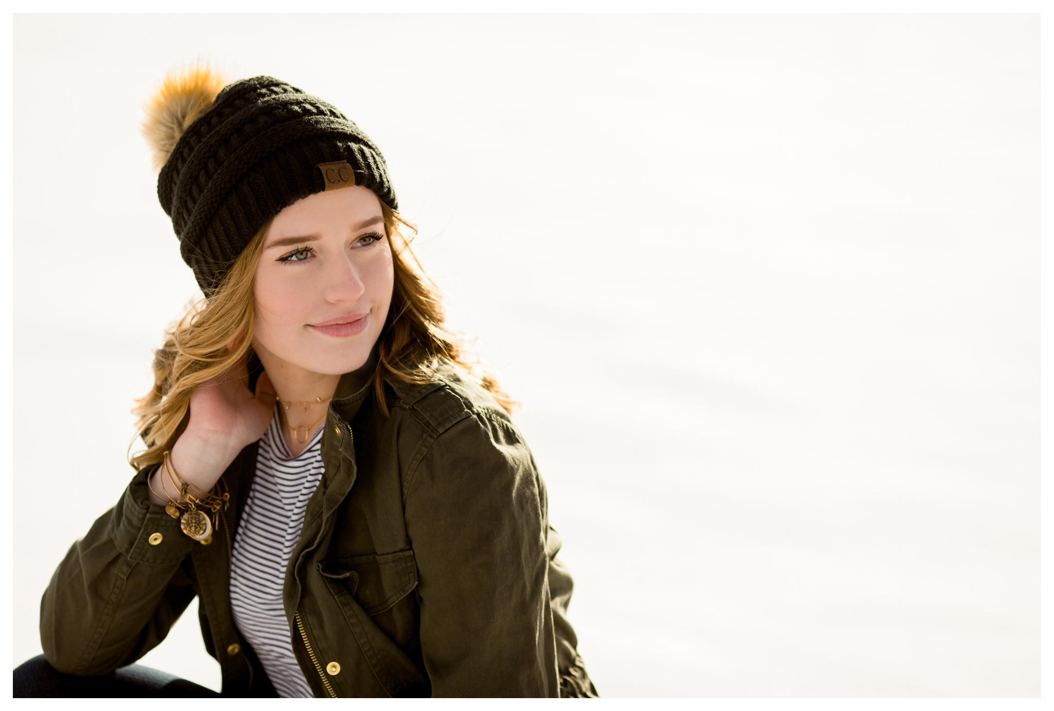 teen girl in stocking cap and army green jacket sitting in the snow at Colorado winter senior portraits 