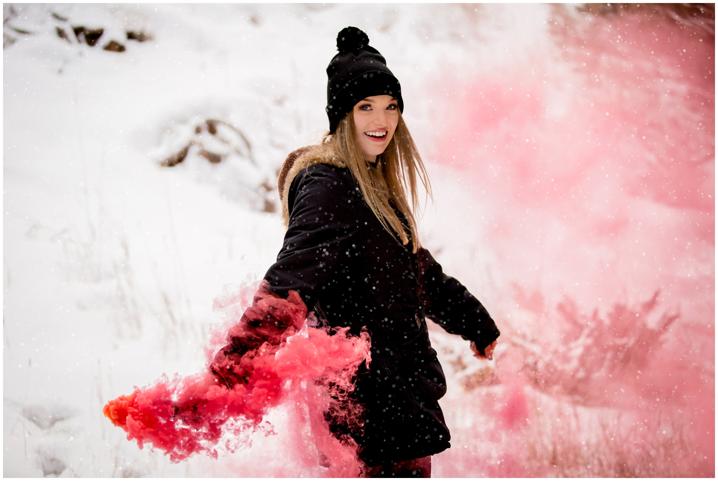teen waving pink smoke bomb in the snow during Colorado winter senior portraits 