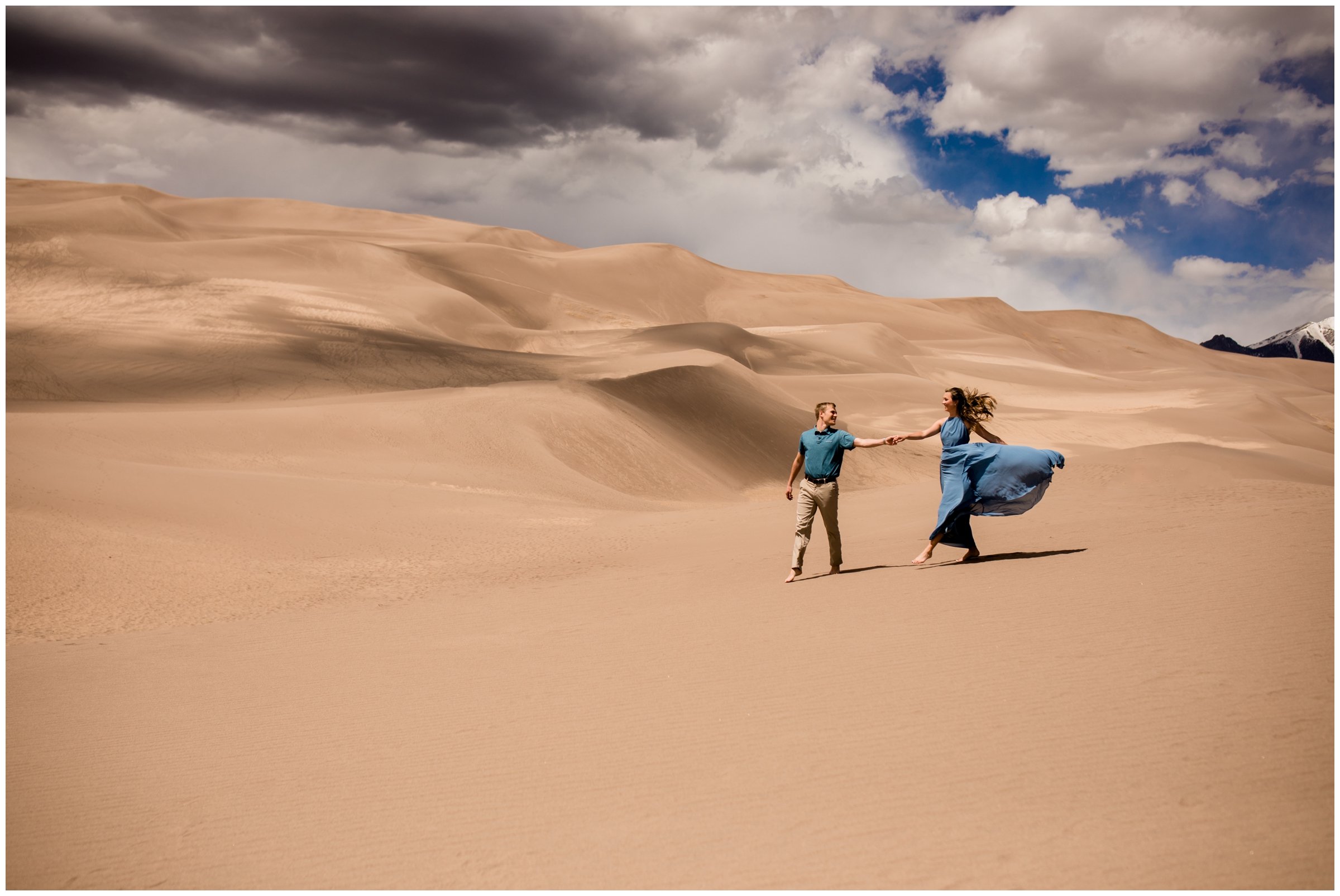 couple walking across sand dunes barefoot during Colorado adventure engagement pictures 