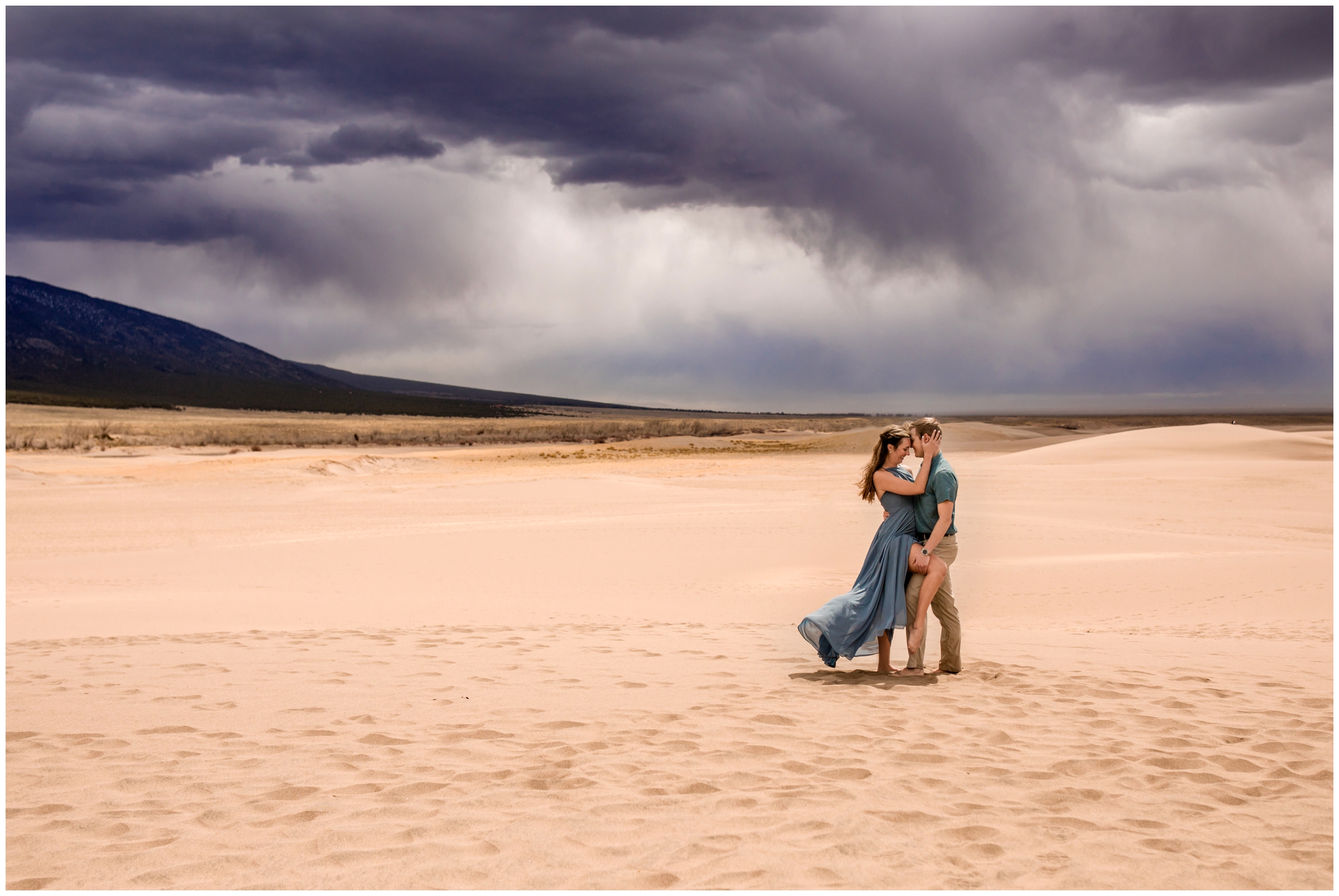 couple embracing under rain clouds at sand dunes Colorado engagement photos 