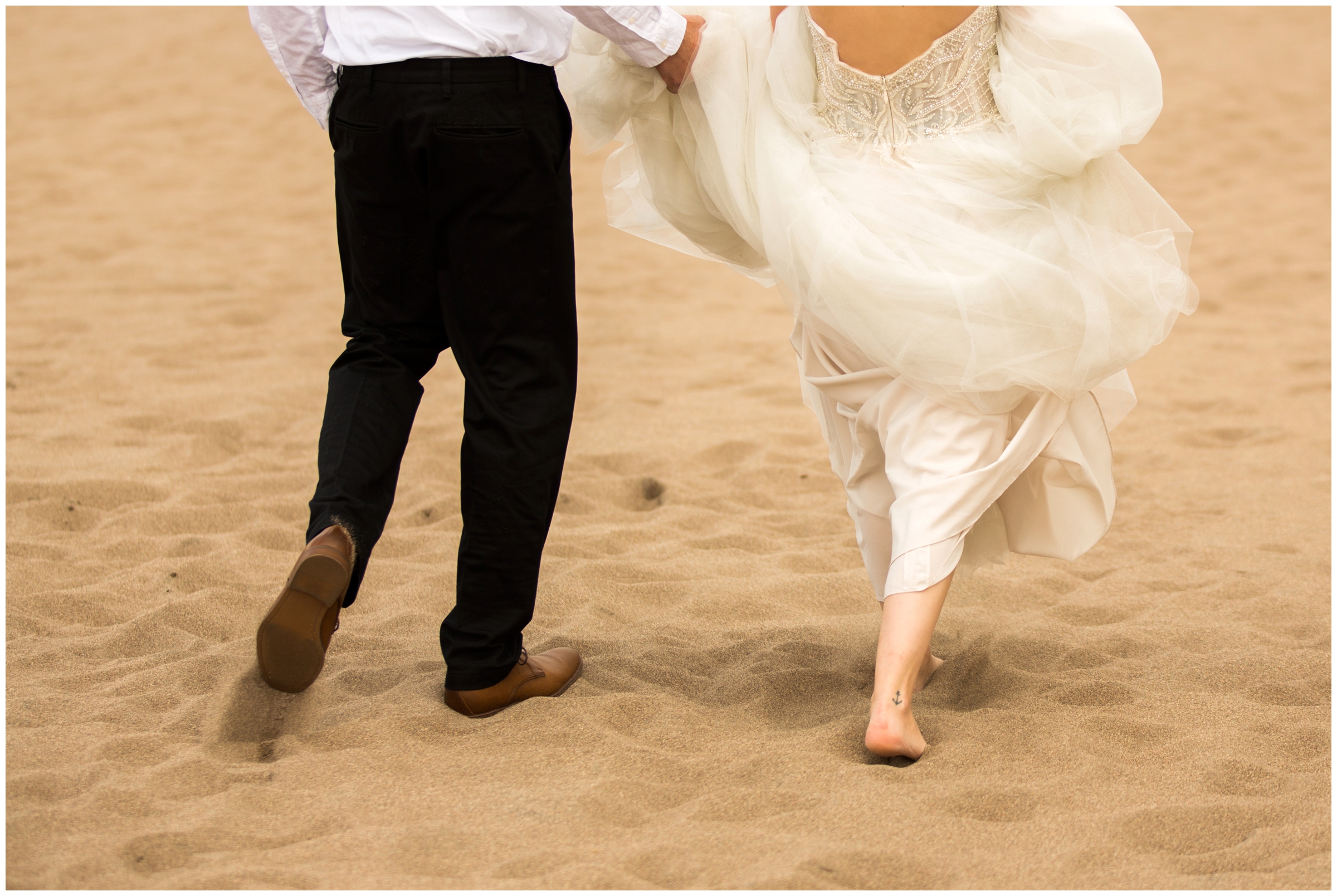 groom holding bride's dress as they walk on the beach