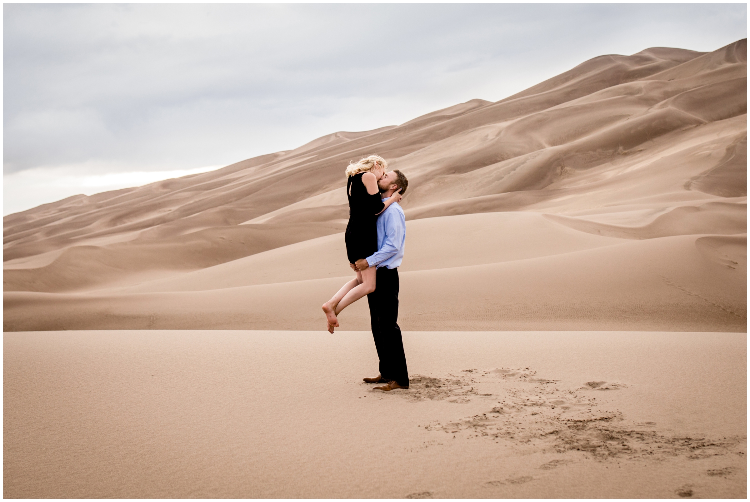 guy lifting fiancé with sand dunes in background at Colorado engagement photography session 