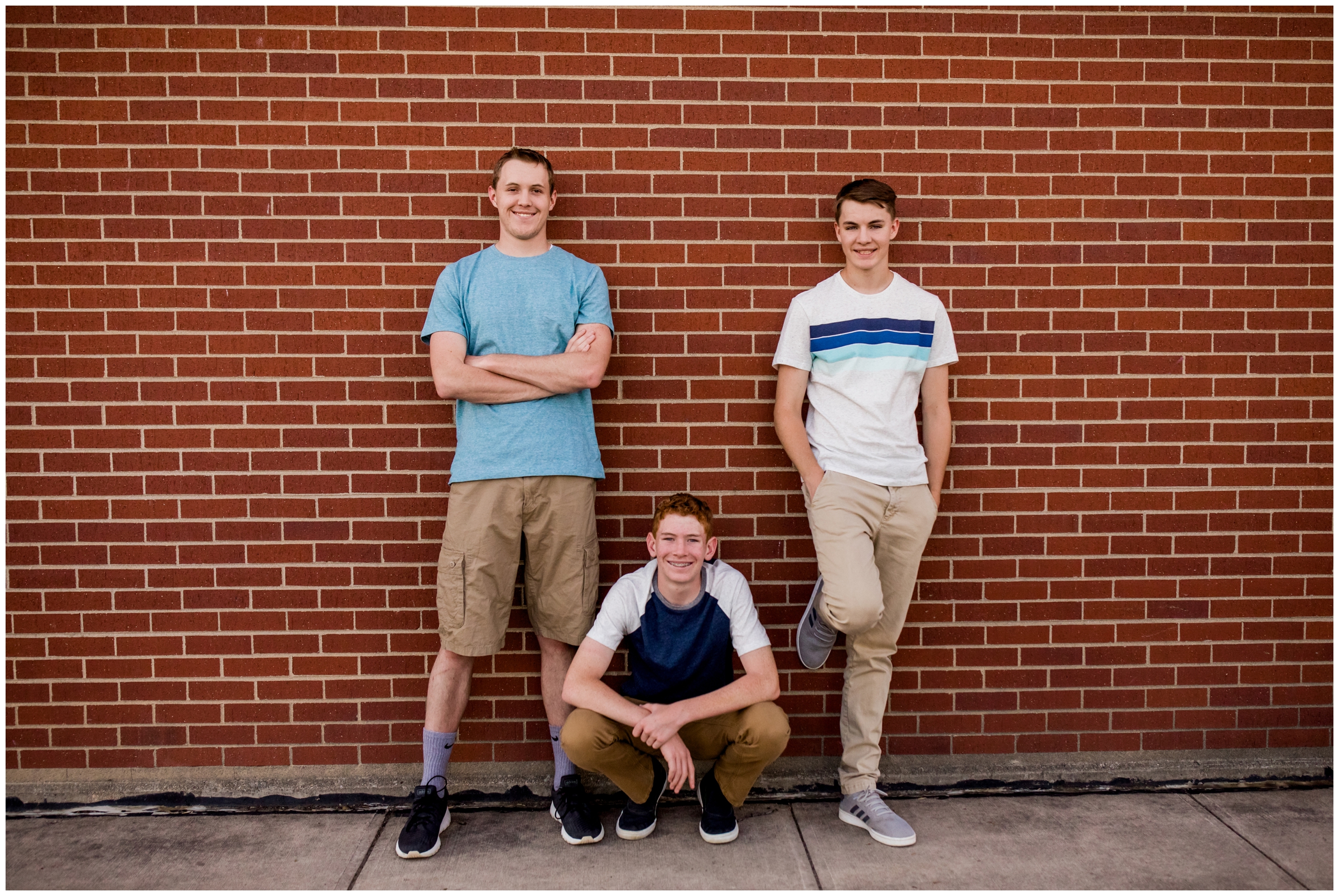 teen brothers posing against brick wall during urban Colorado family portraits