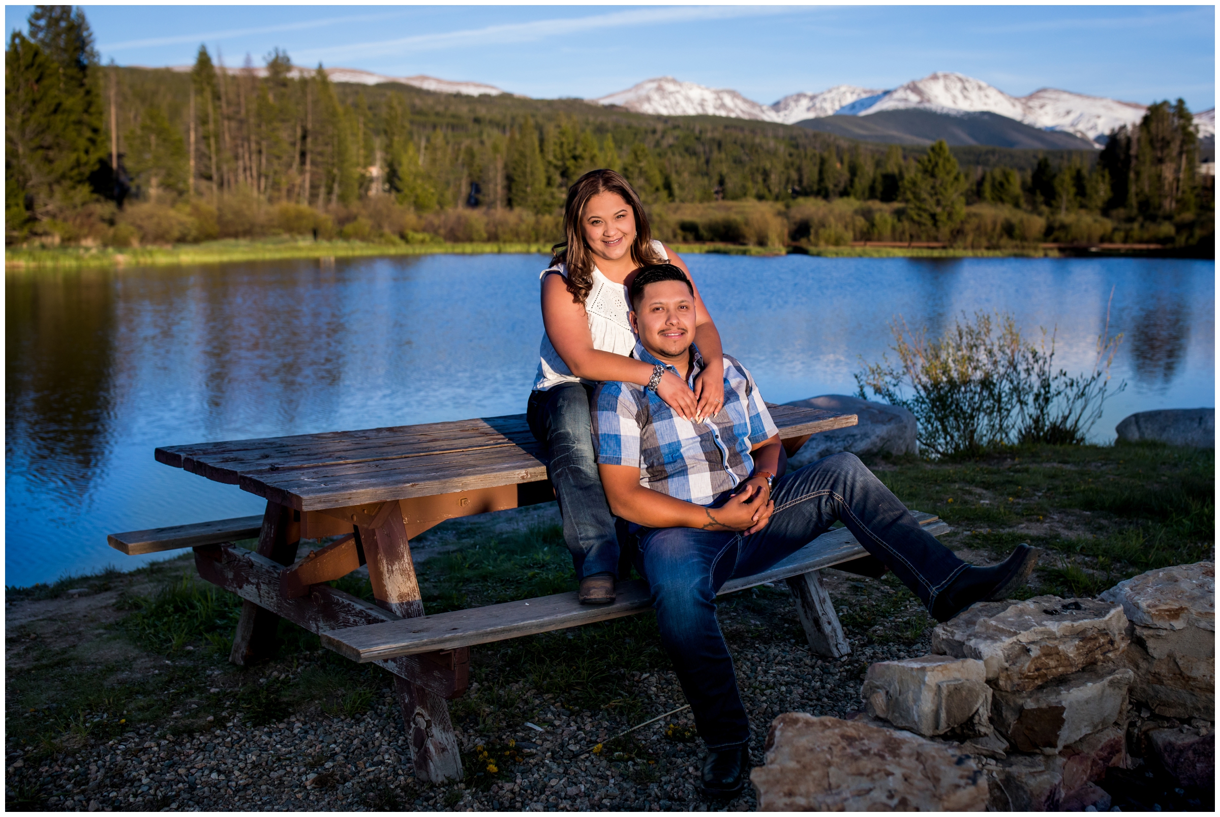 couple posing on picnic bench with mountains in background during Grand County Colorado engagement pictures 