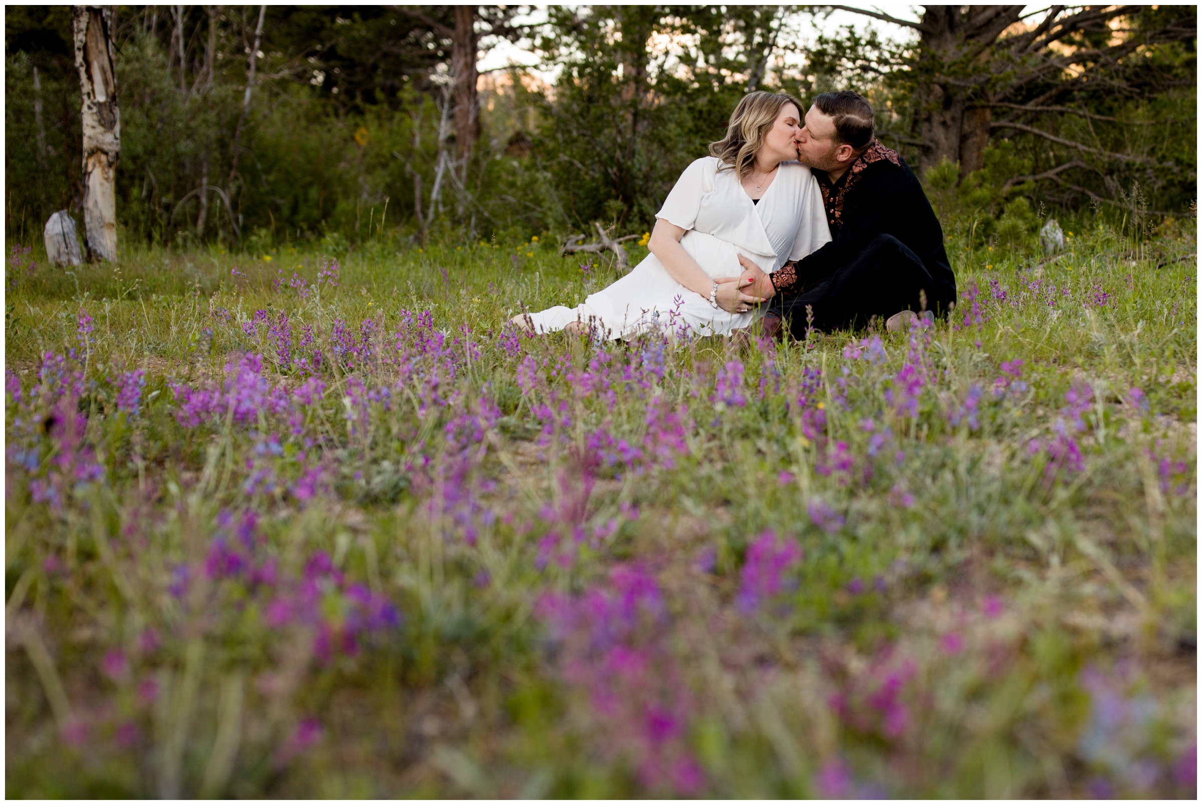 couple sitting in flower field during Colorado summer maternity photographs 