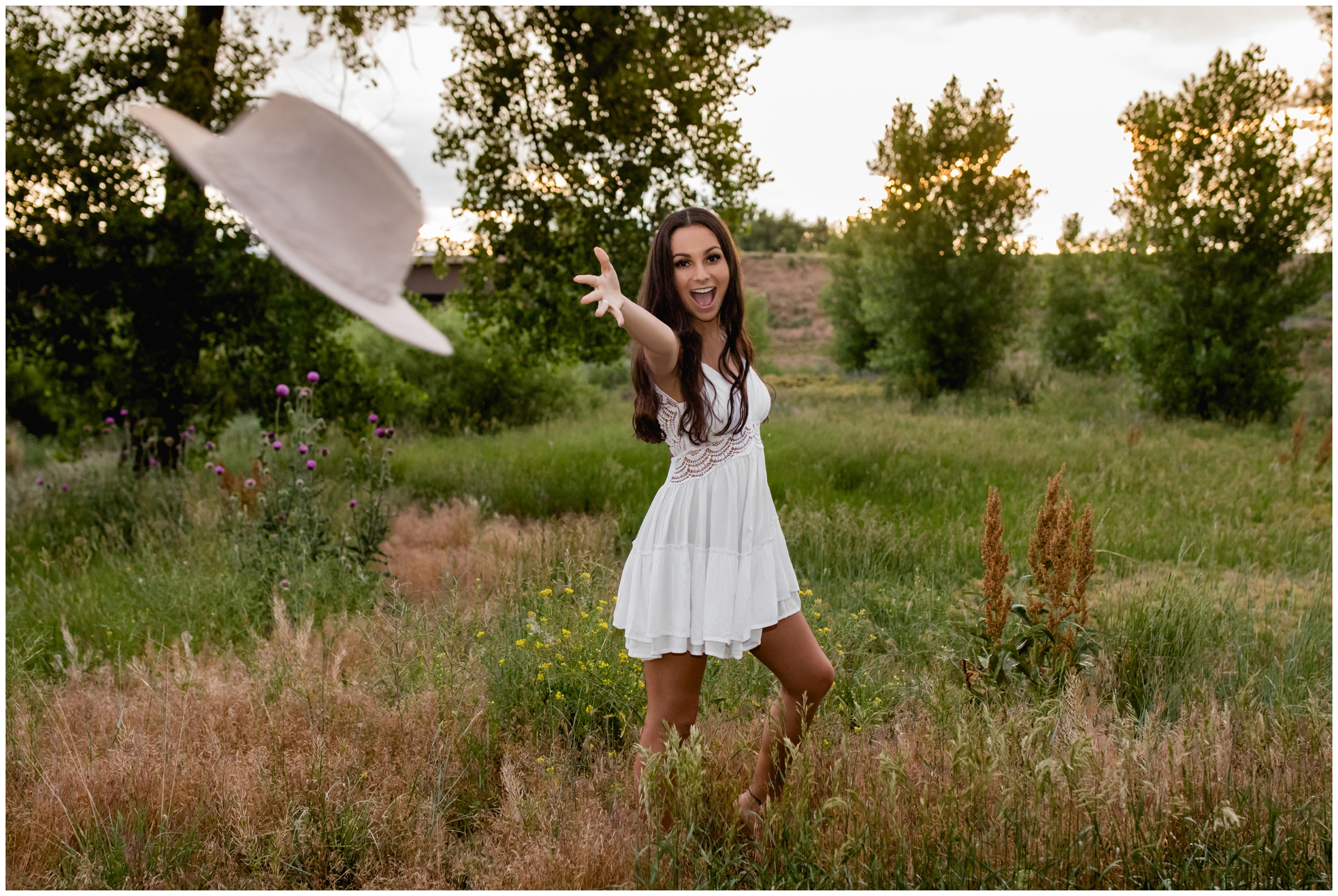 teen girl in white dress throwing hat during unique Colorado senior photography session 