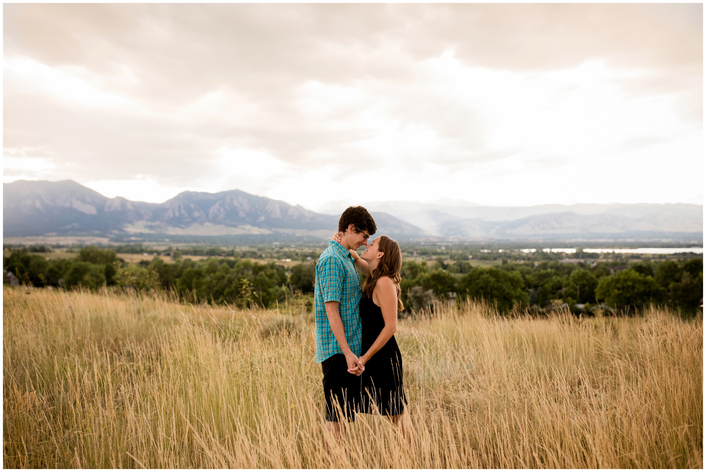 couple standing in a field with flatirons in background during Boulder Colorado engagement photography 