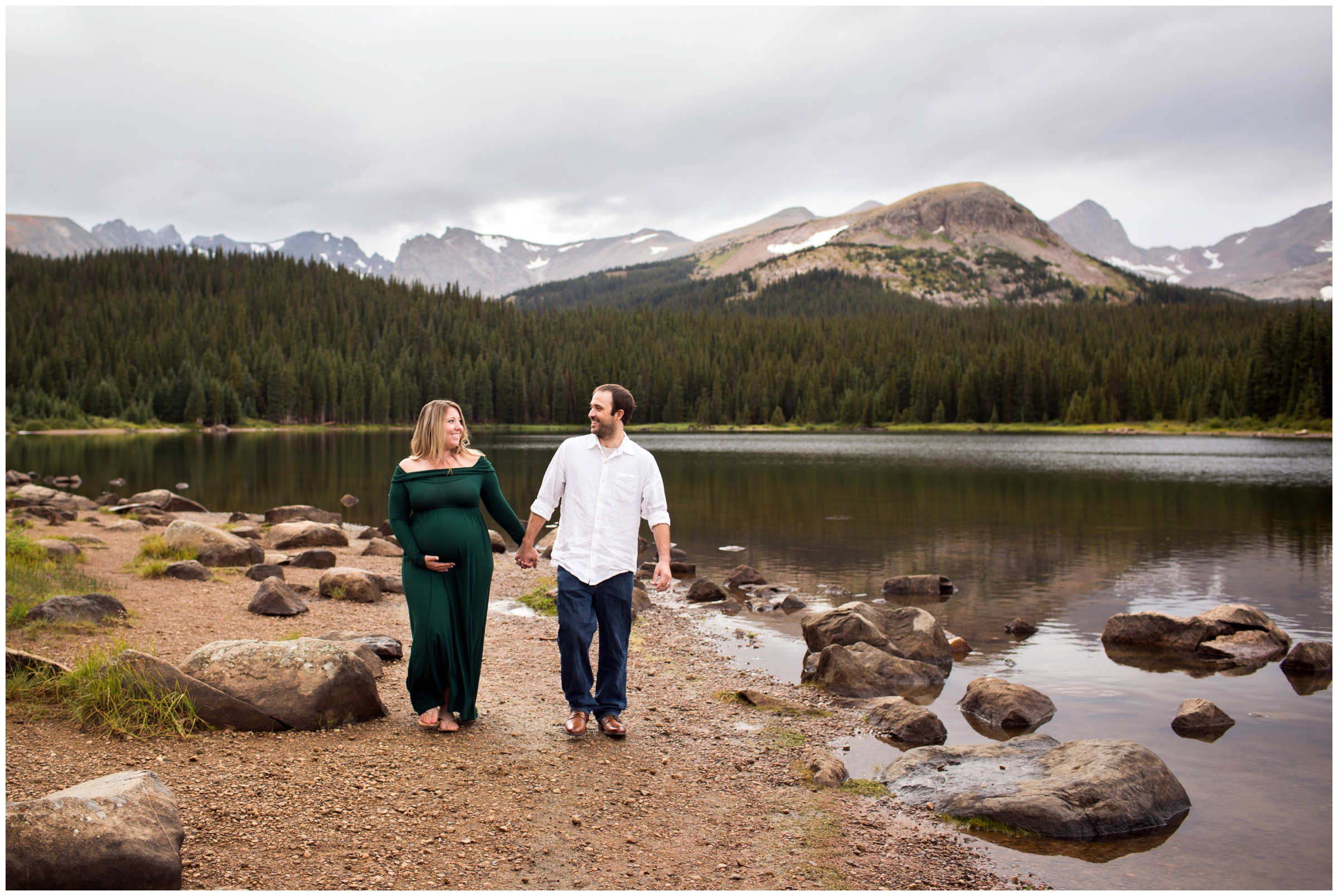 couple walking against lakes edge during Colorado mountain maternity photos 