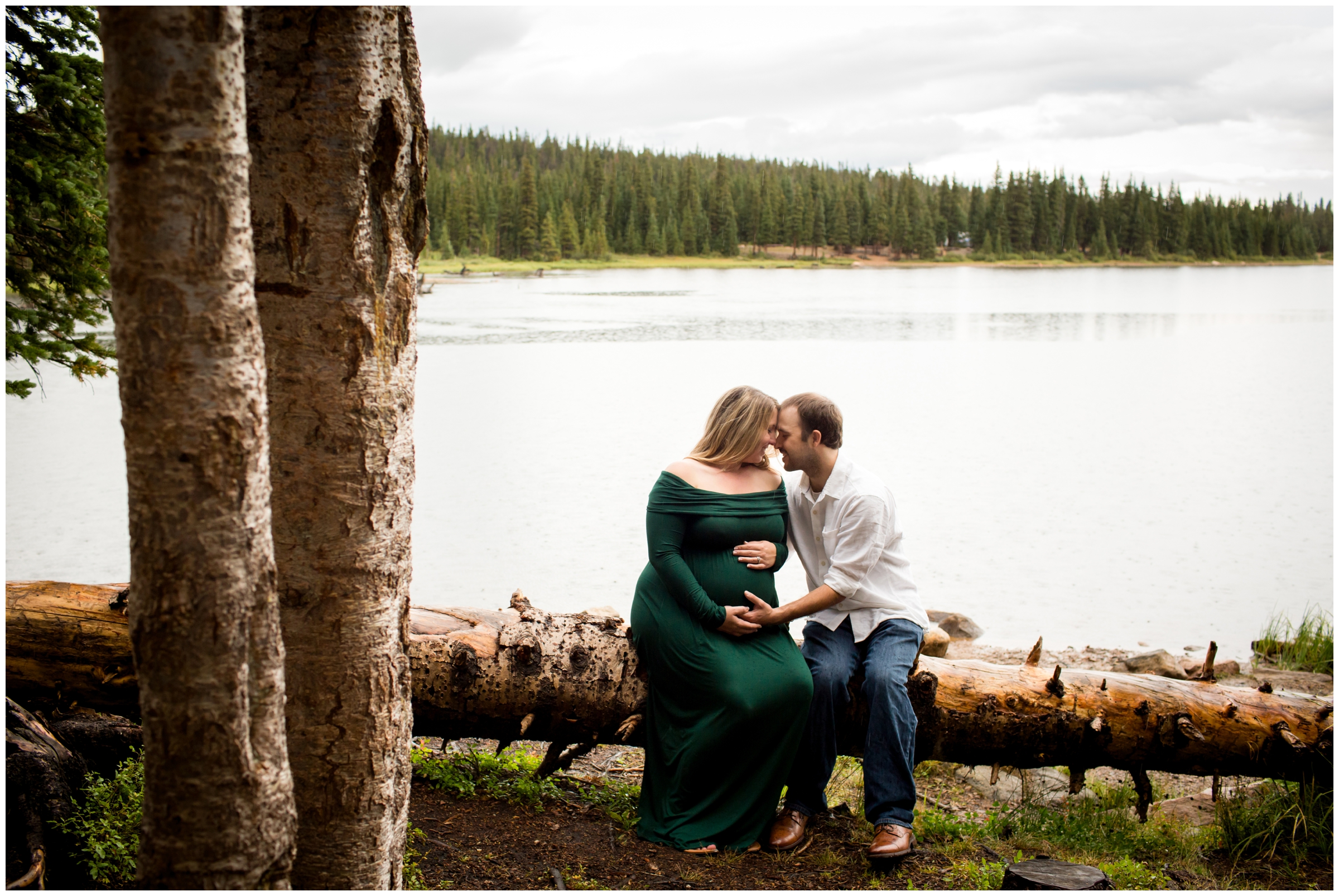 couple sitting on log with a lake behind during CO pregnancy pictures 