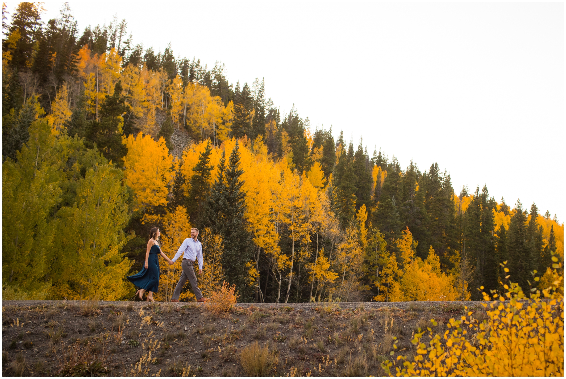 couple walking with colorful fall foliage in background at Breckenridge Sawmill Museum engagement portraits 
