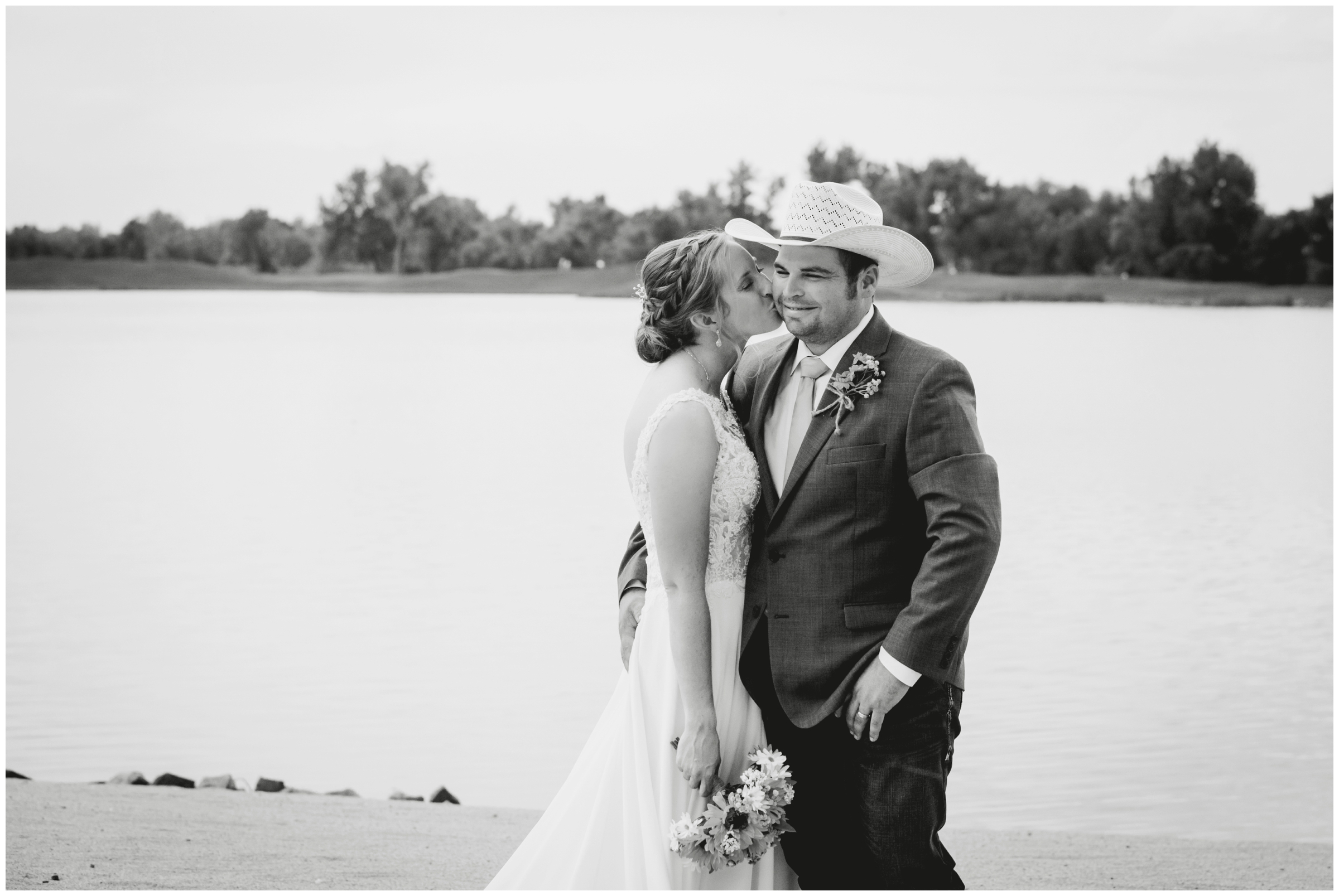 bride and groom kissing at the water's edge during windsor Colorado lake wedding pictures 