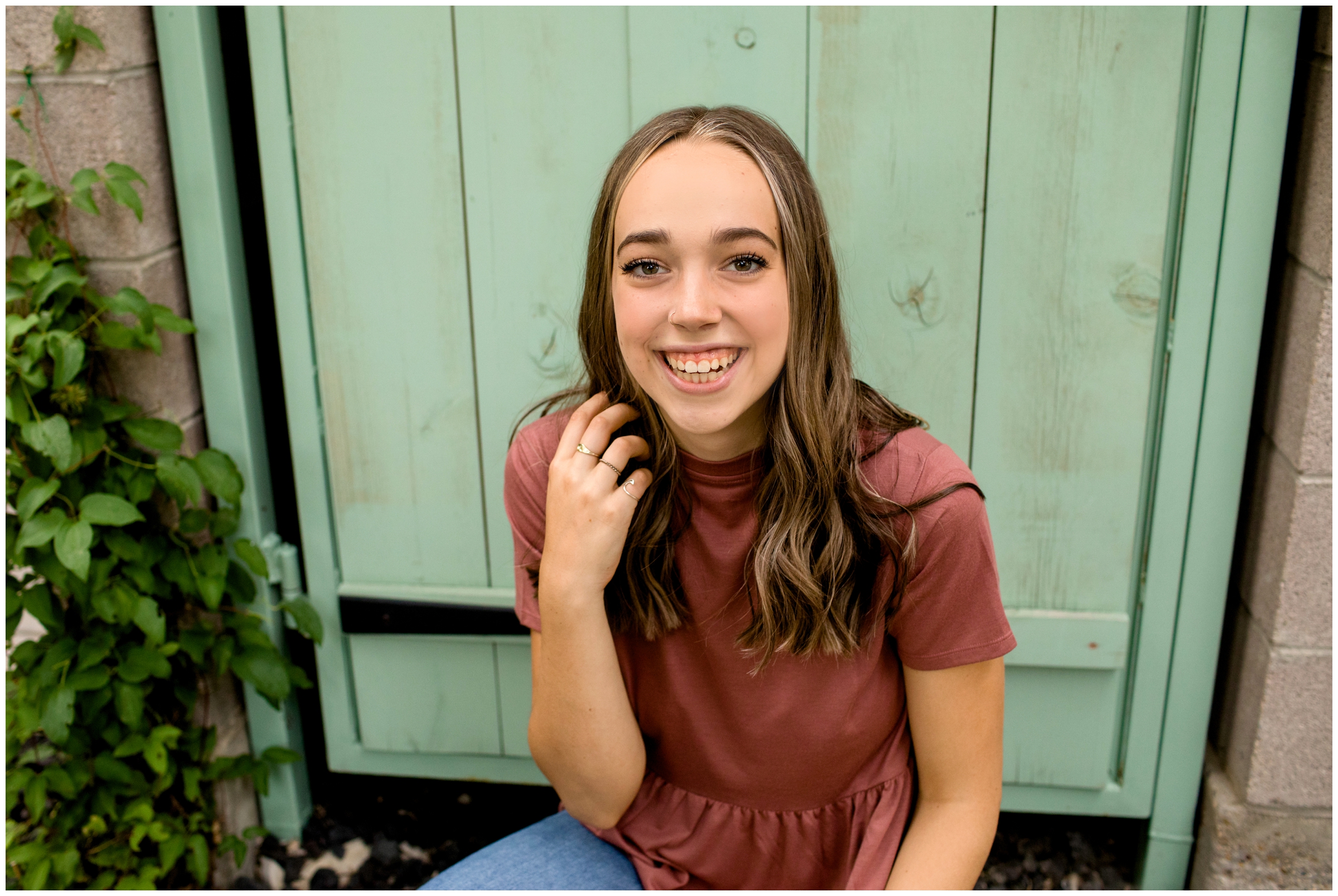 teen sitting against mint green gate during urban senior pictures in Prospect New Town Longmont 