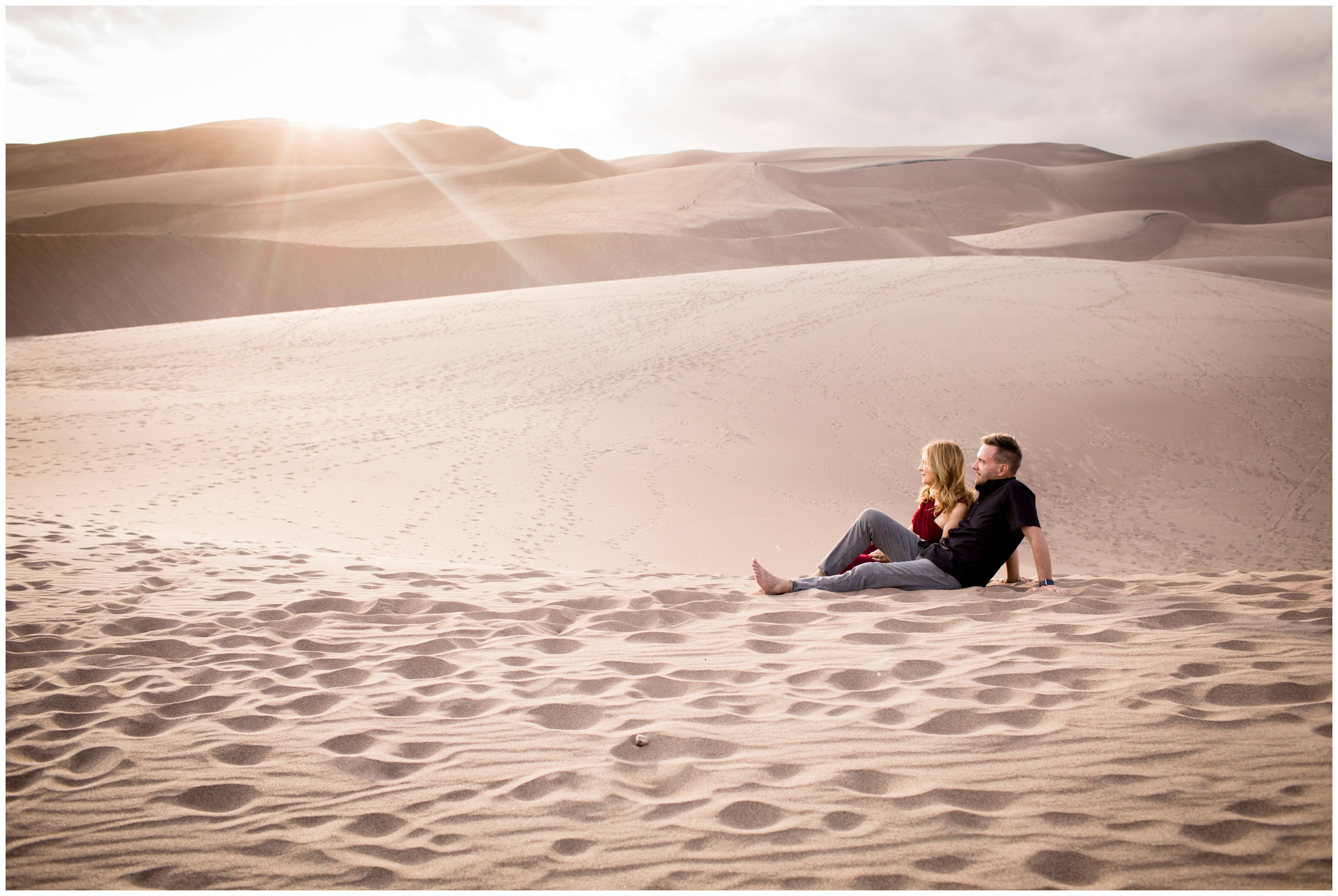 couple sitting on sand dunes during Colorado adventure engagement couple's photography session 