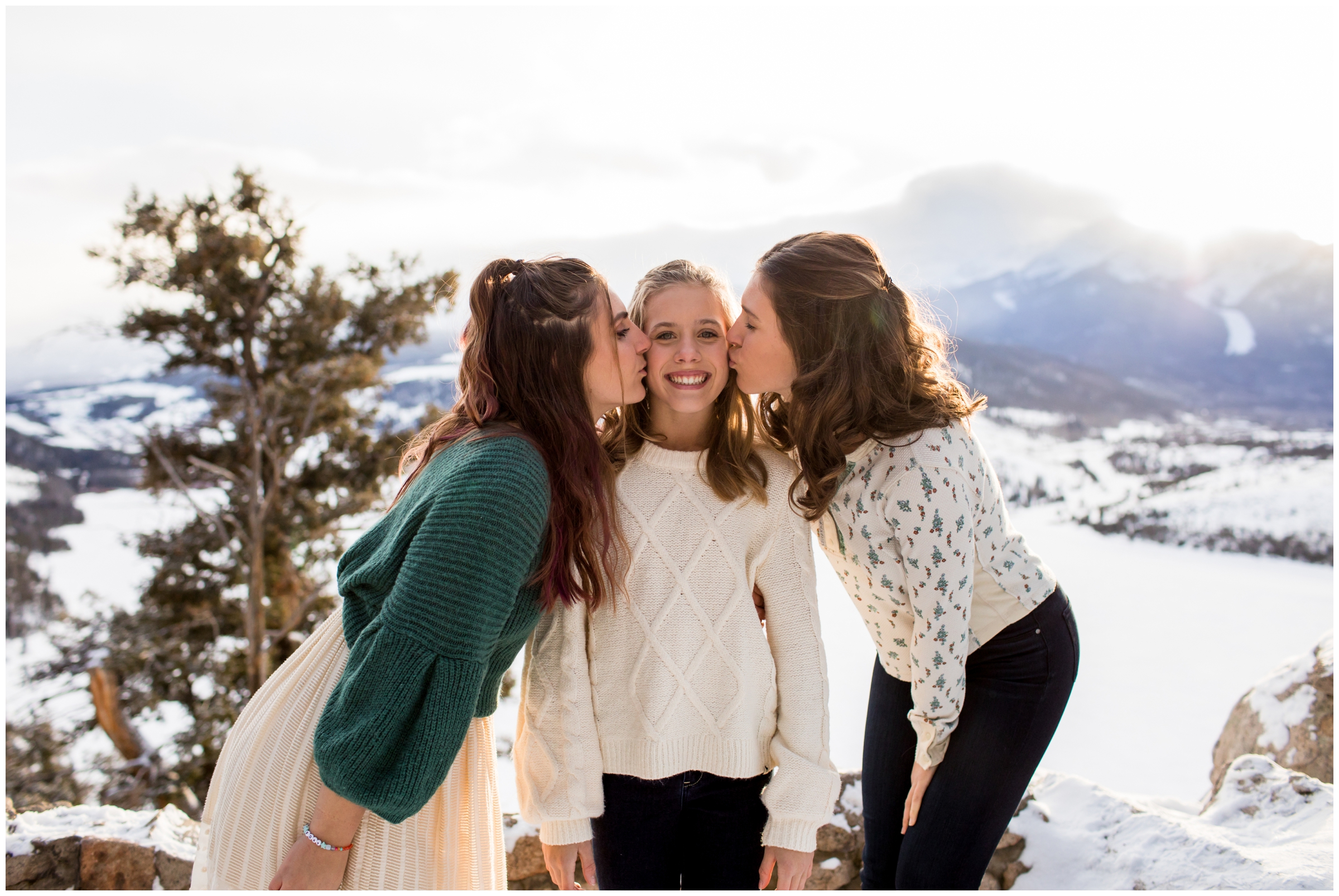 sisters kissing younger sister on cheeks with mountains in background 