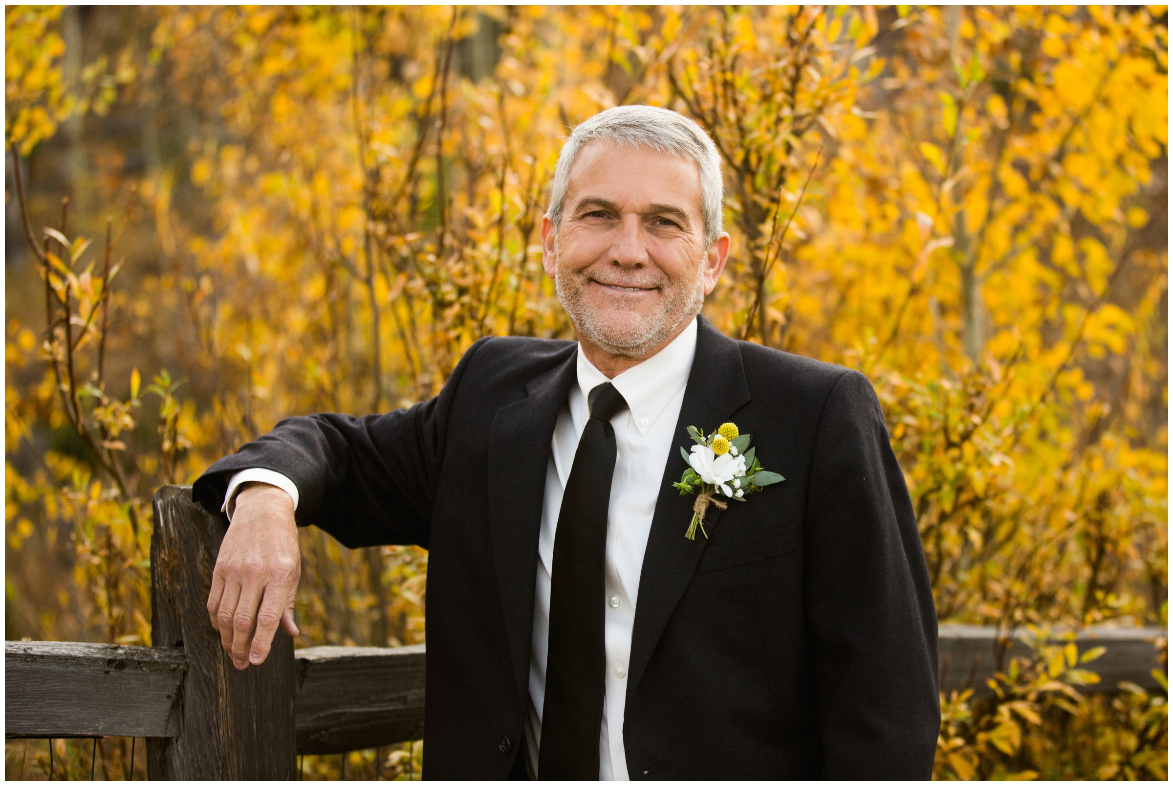 Colorado groom leaning on fence with fall foliage in background