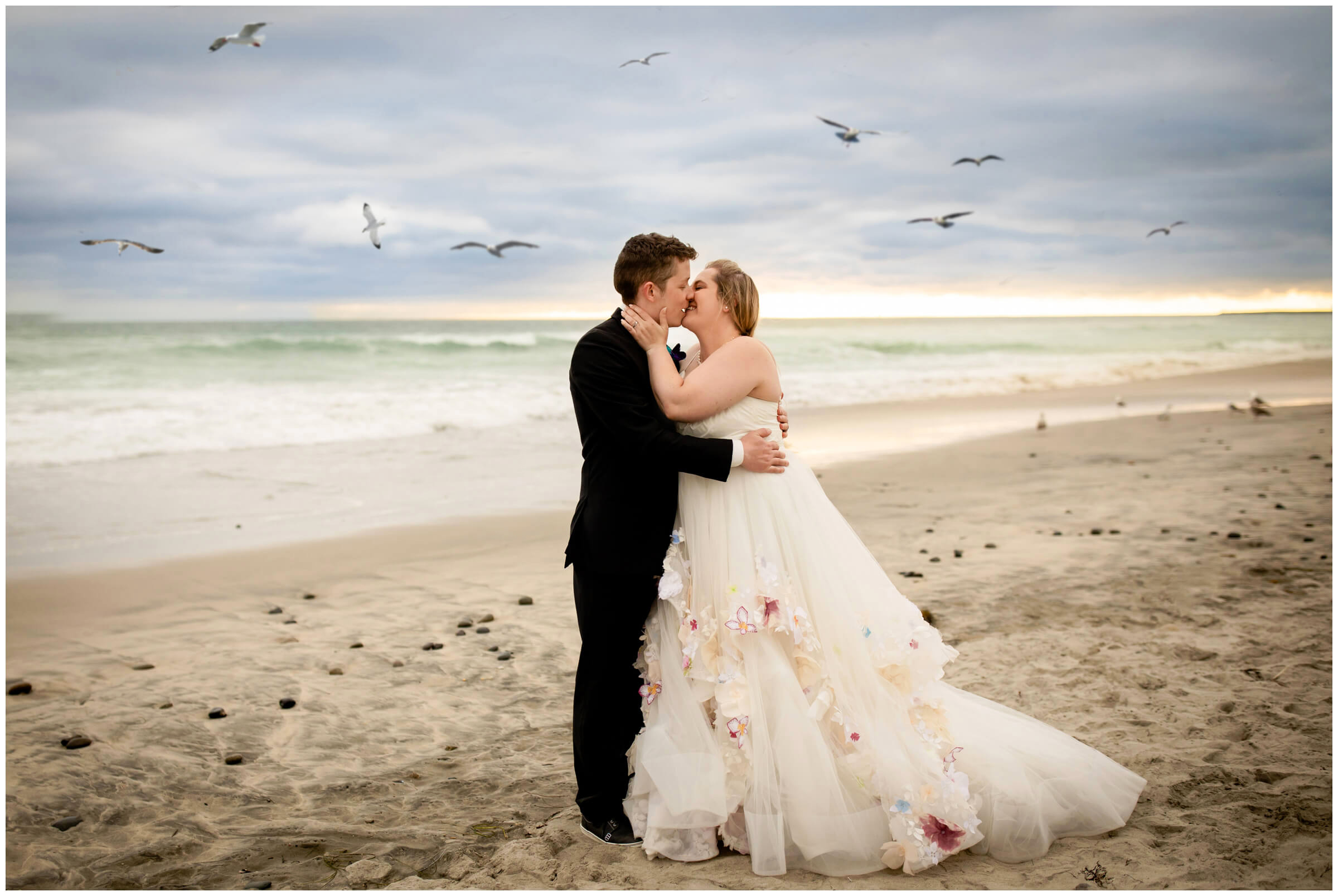 wedding couple kissing on the beach in Carlsbad California while seagulls fly around