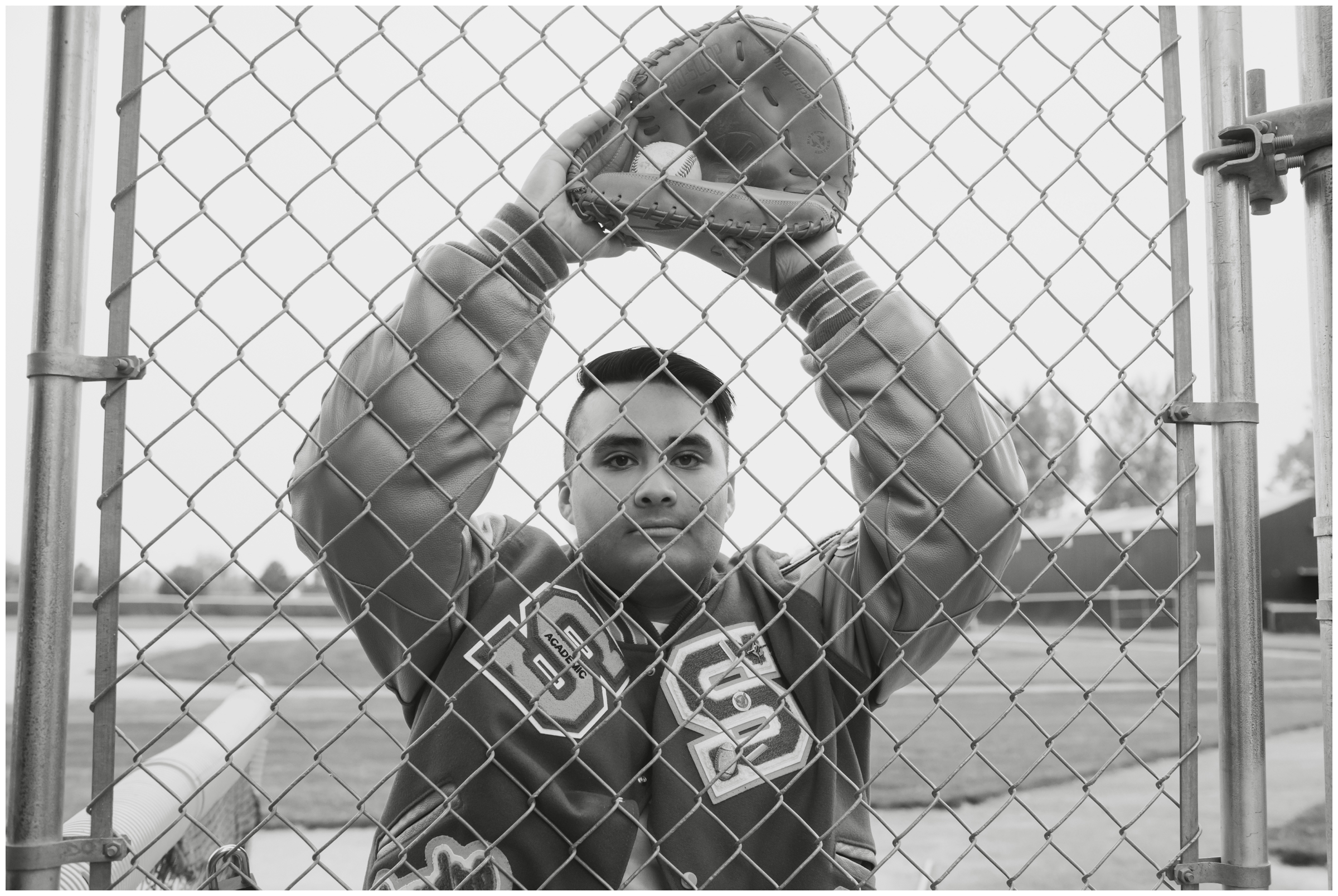 baseball player posing behind chain link fence during unique Colorado senior photos 