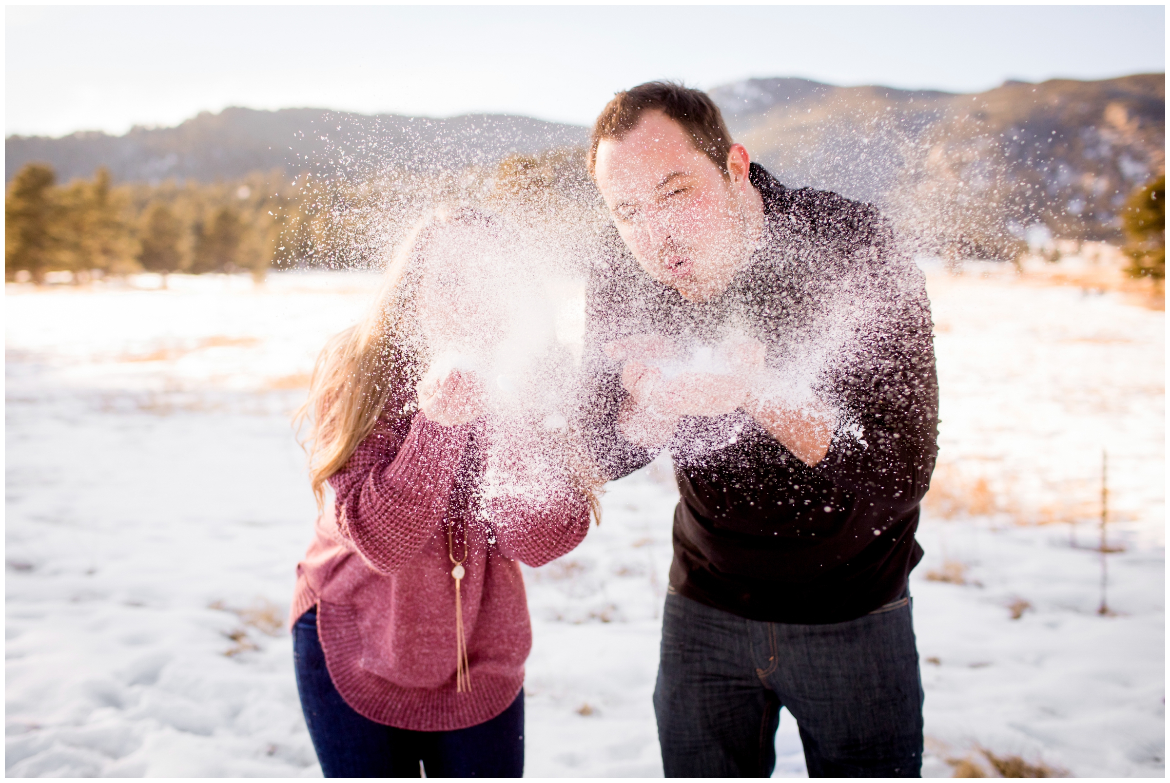 couple blowing snow at camera during Evergreen Colorado winter engagement portraits 