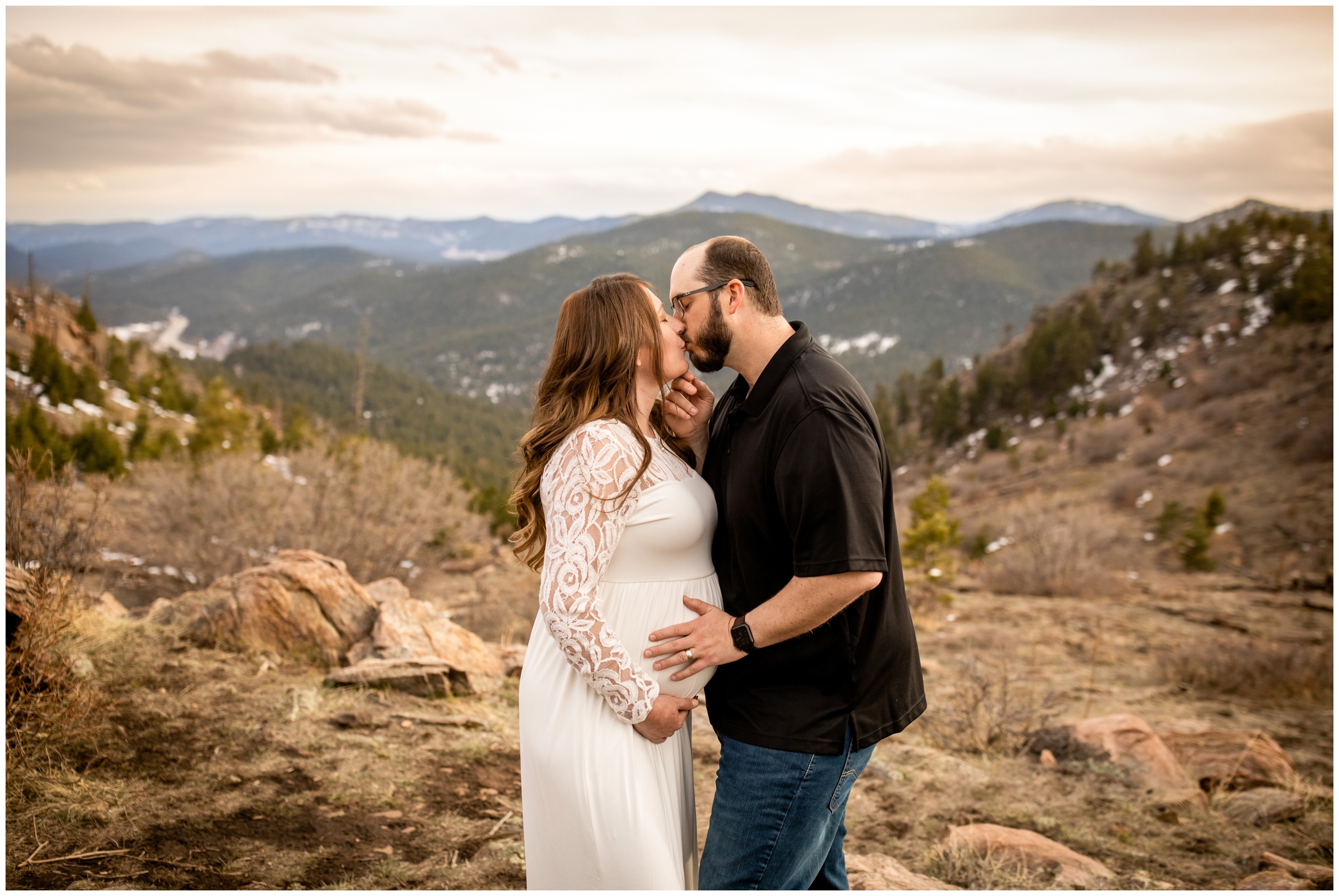 Couple kissing with mountains in background during Colorado spring maternity photography session 