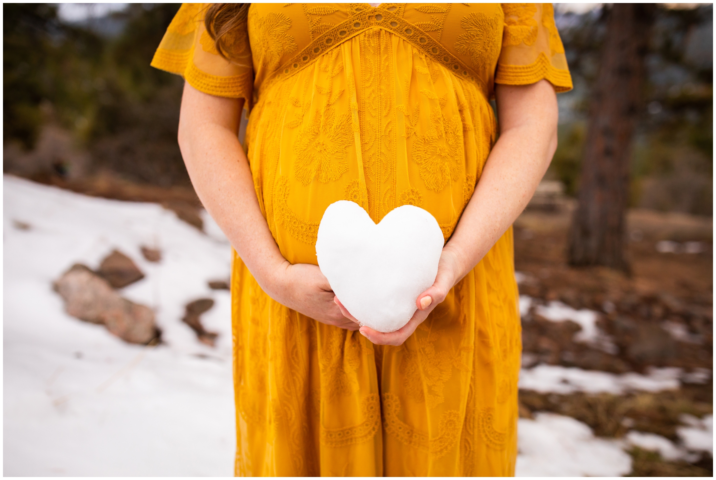 Pregnant woman holding heart snow ball against her belly during winter pregnancy portraits 