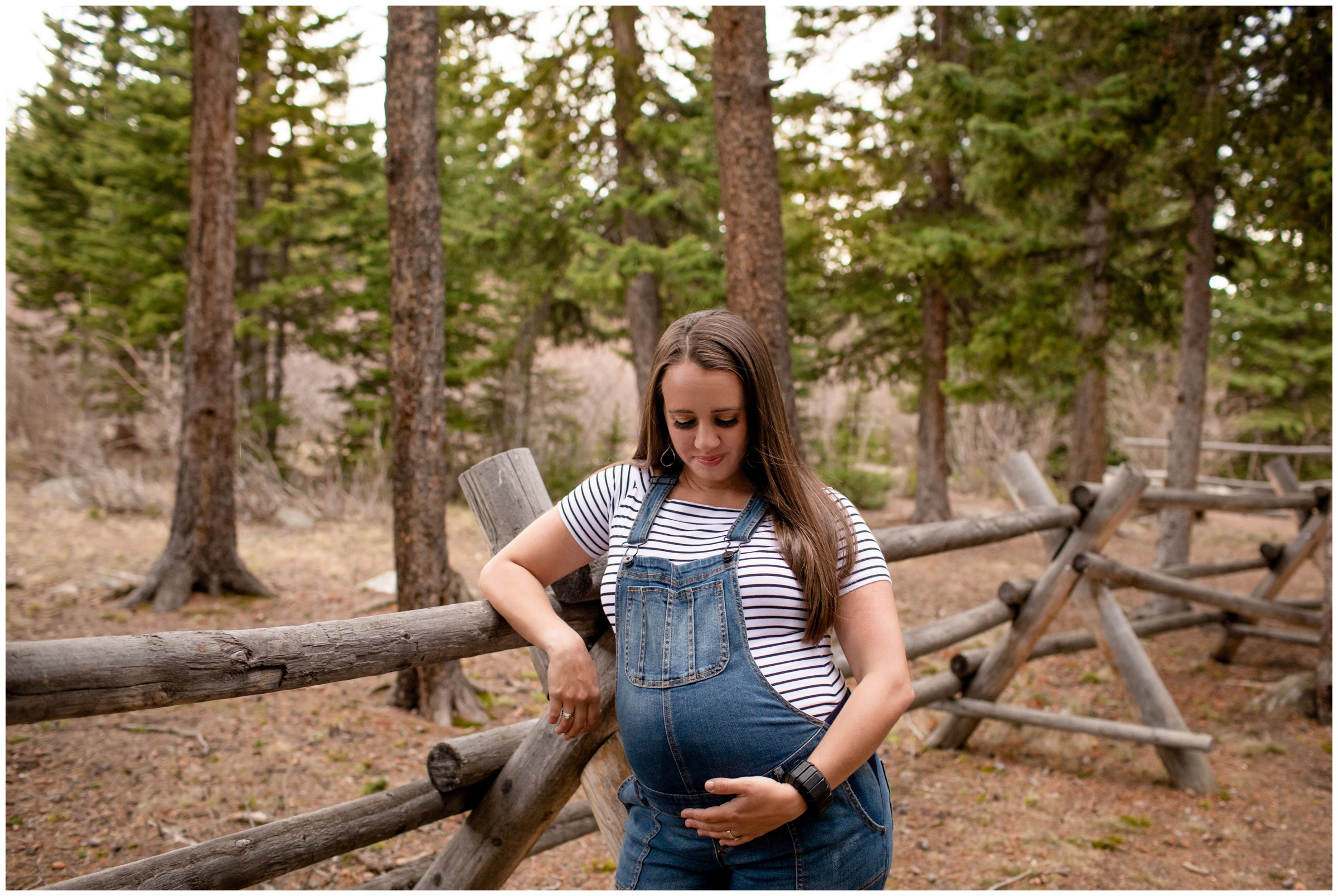 Pregnant woman in overalls leaning on wooden fence during Colorado mountain maternity portraits by plum pretty photography 