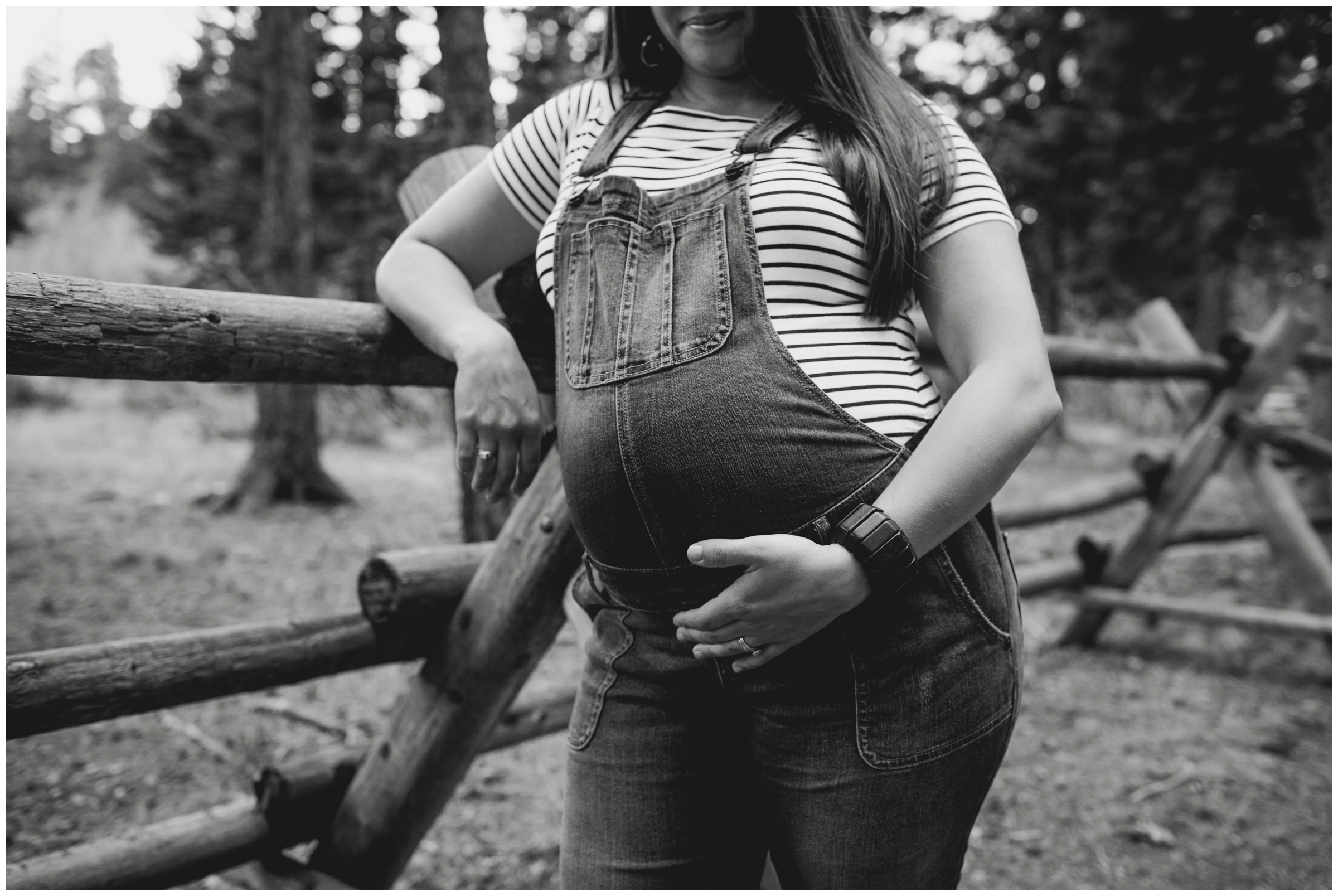 Pregnant woman in cute Maternity overalls leaning against wooden fence