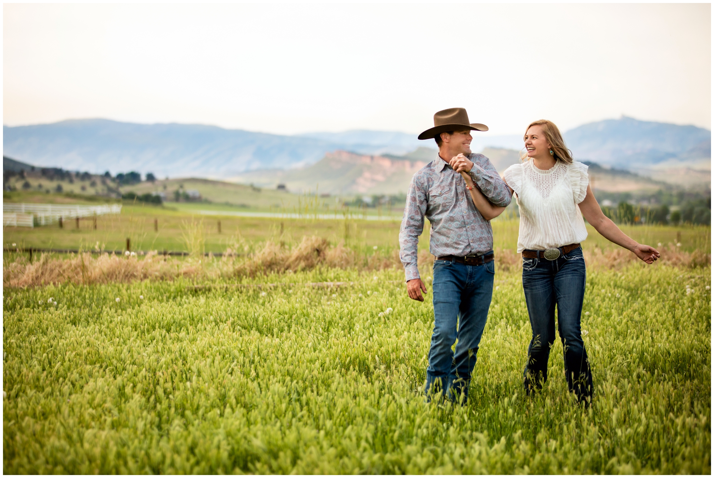 couple walking through field with mountains in background during Northern Colorado couples photos on private farmland 