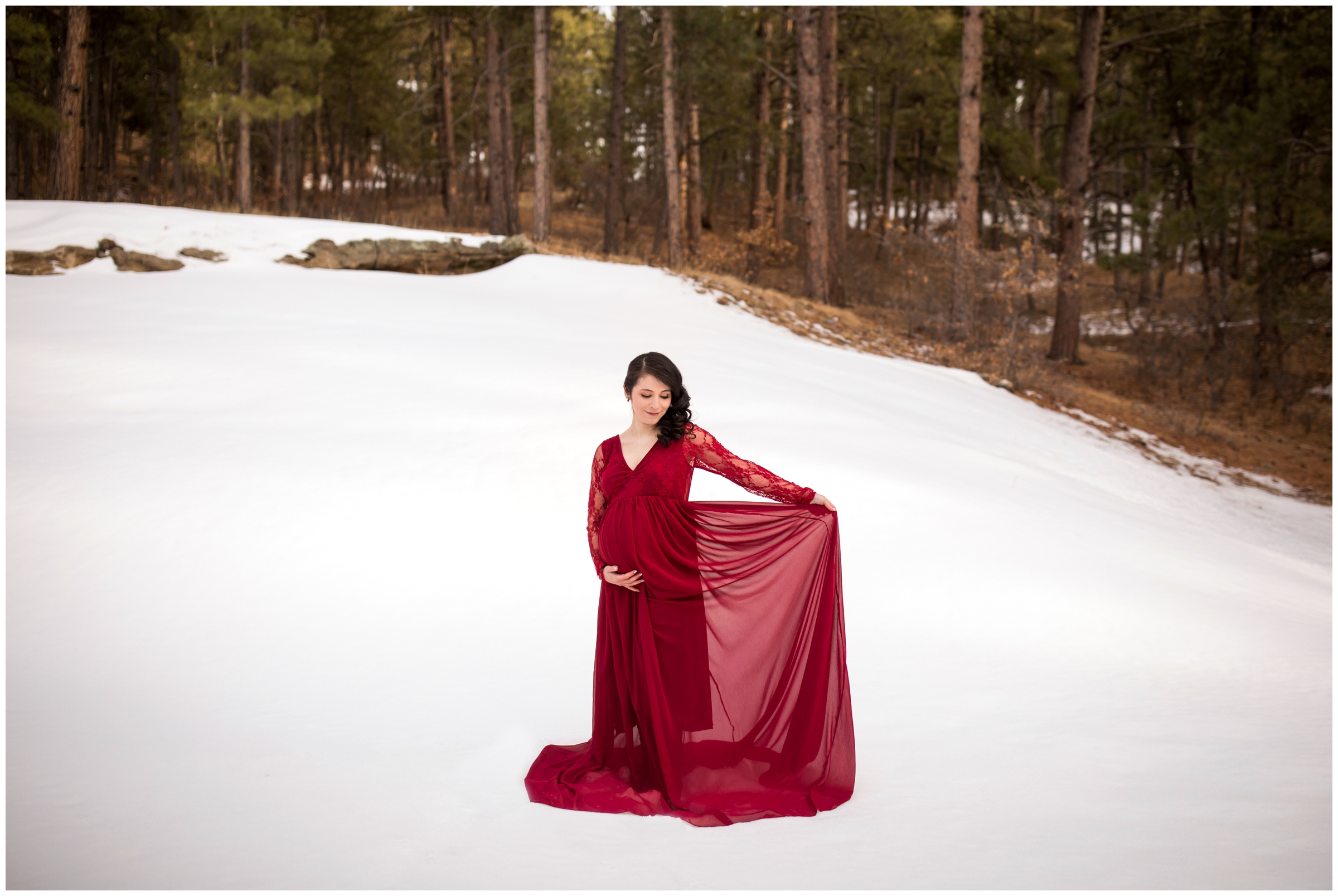 woman in red dress posing in the snow during Colorado winter maternity portraits