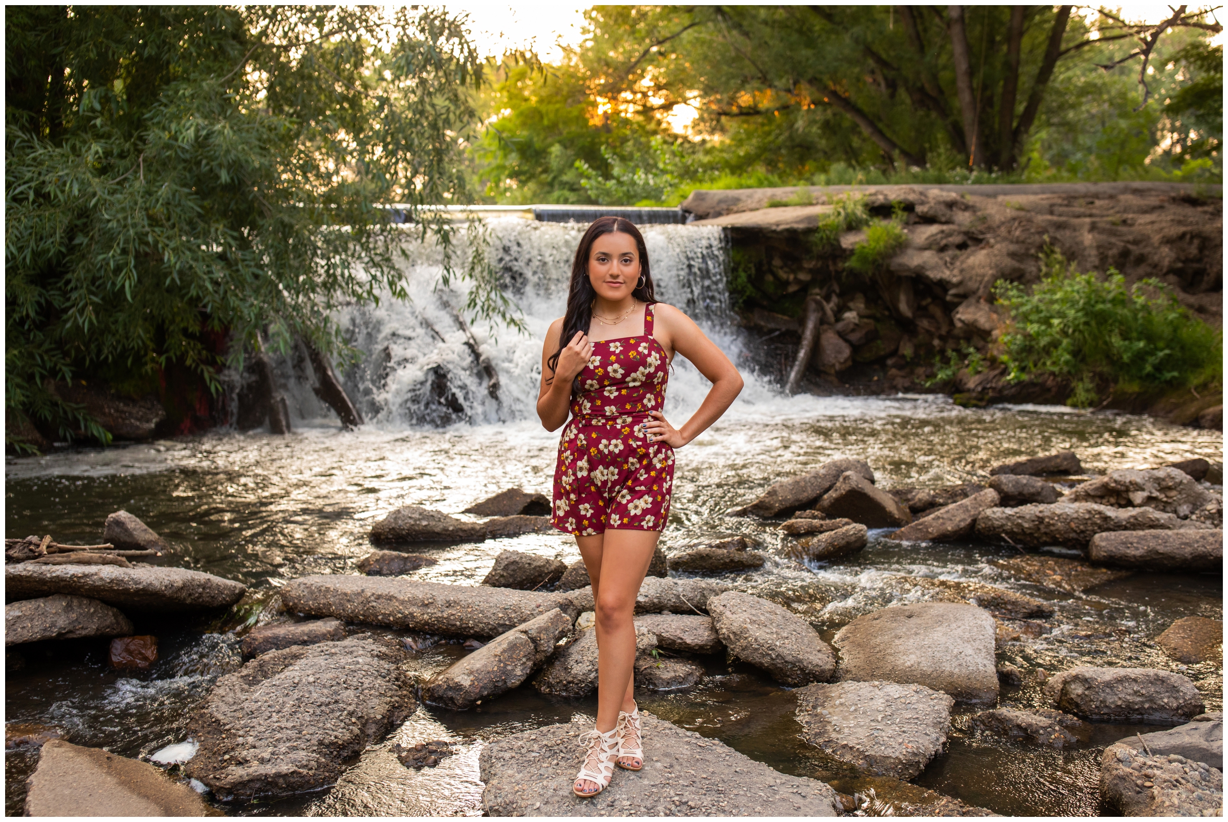 teen in floral romper posing in front of waterfall during Colorado senior portraits 