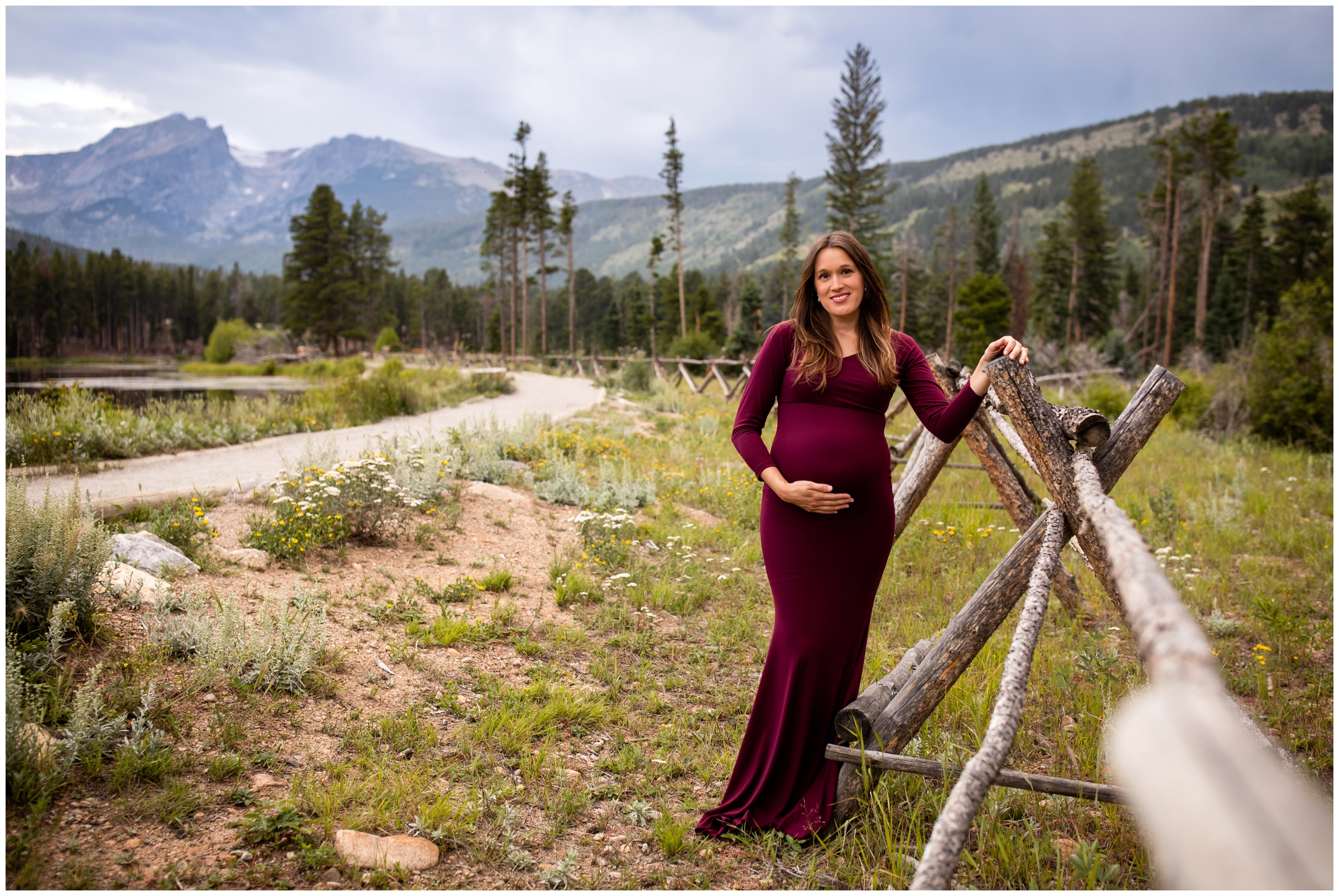 pregnant woman leaning on wooden fence at Sprague Lake in Estes Park