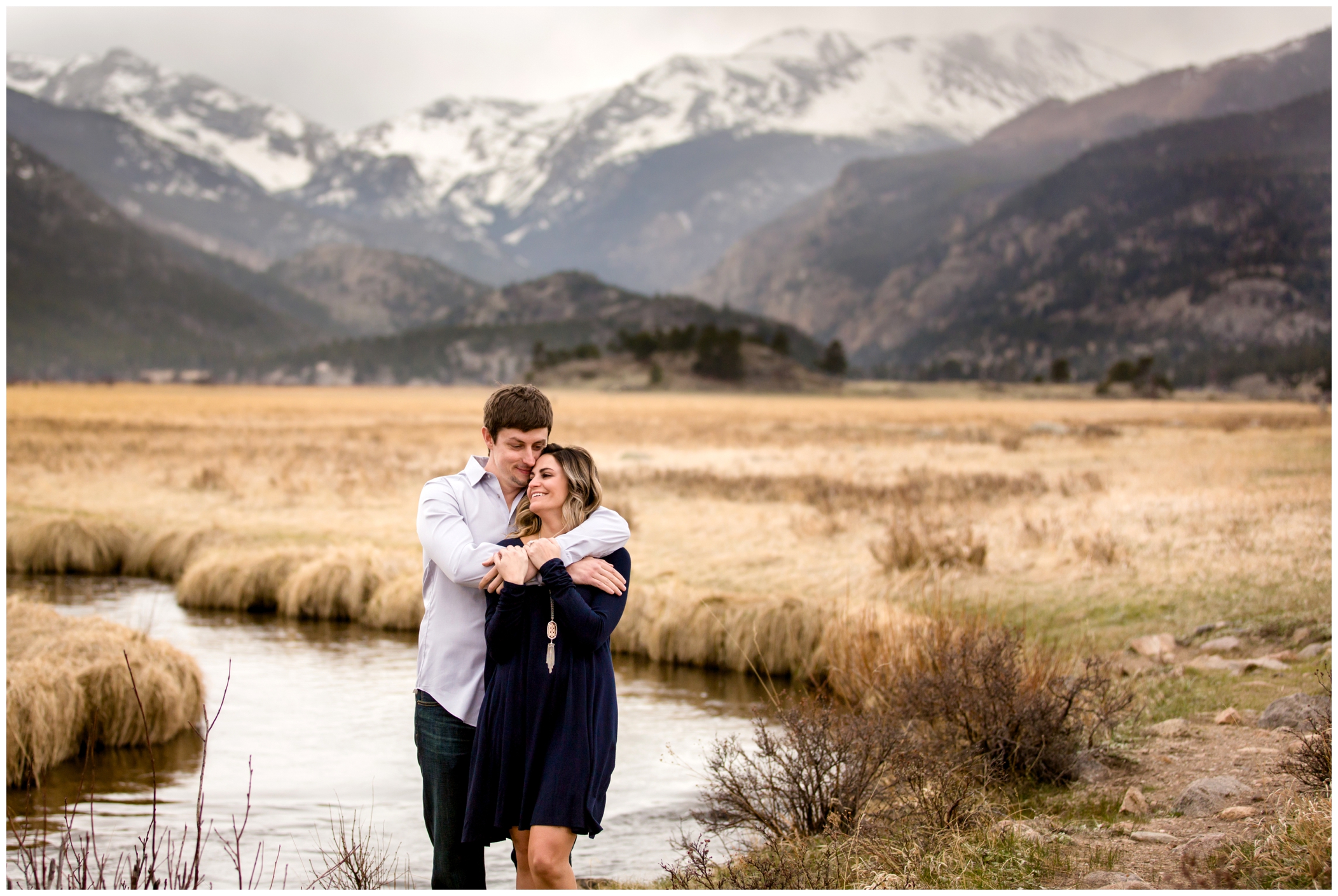 couple hugging with mountain in the background during their estes park engagement photography session in RMNP