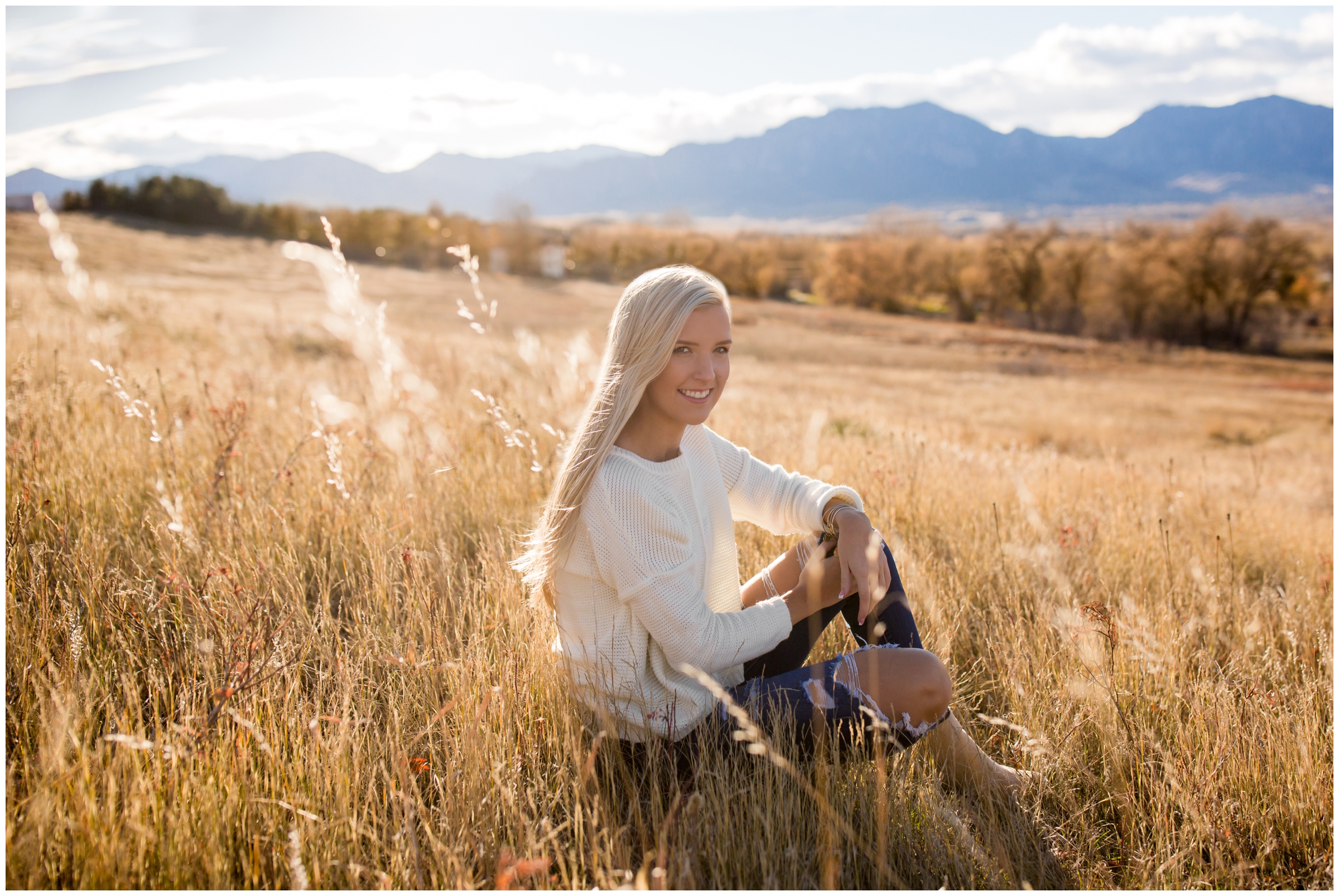 teen girl sitting in field with flatirons in background at Erie High senior photos at Davidson Mesa Louisville Colorado