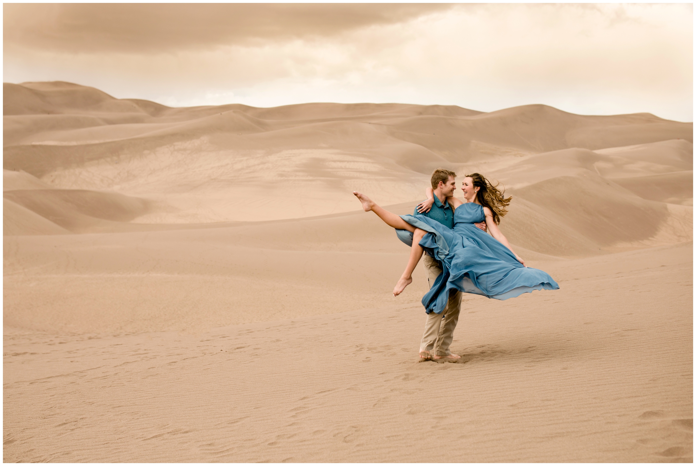 guy spinning woman in blue dress at Colorado Great Sand Dunes engagement photography session with Plum Pretty Photography