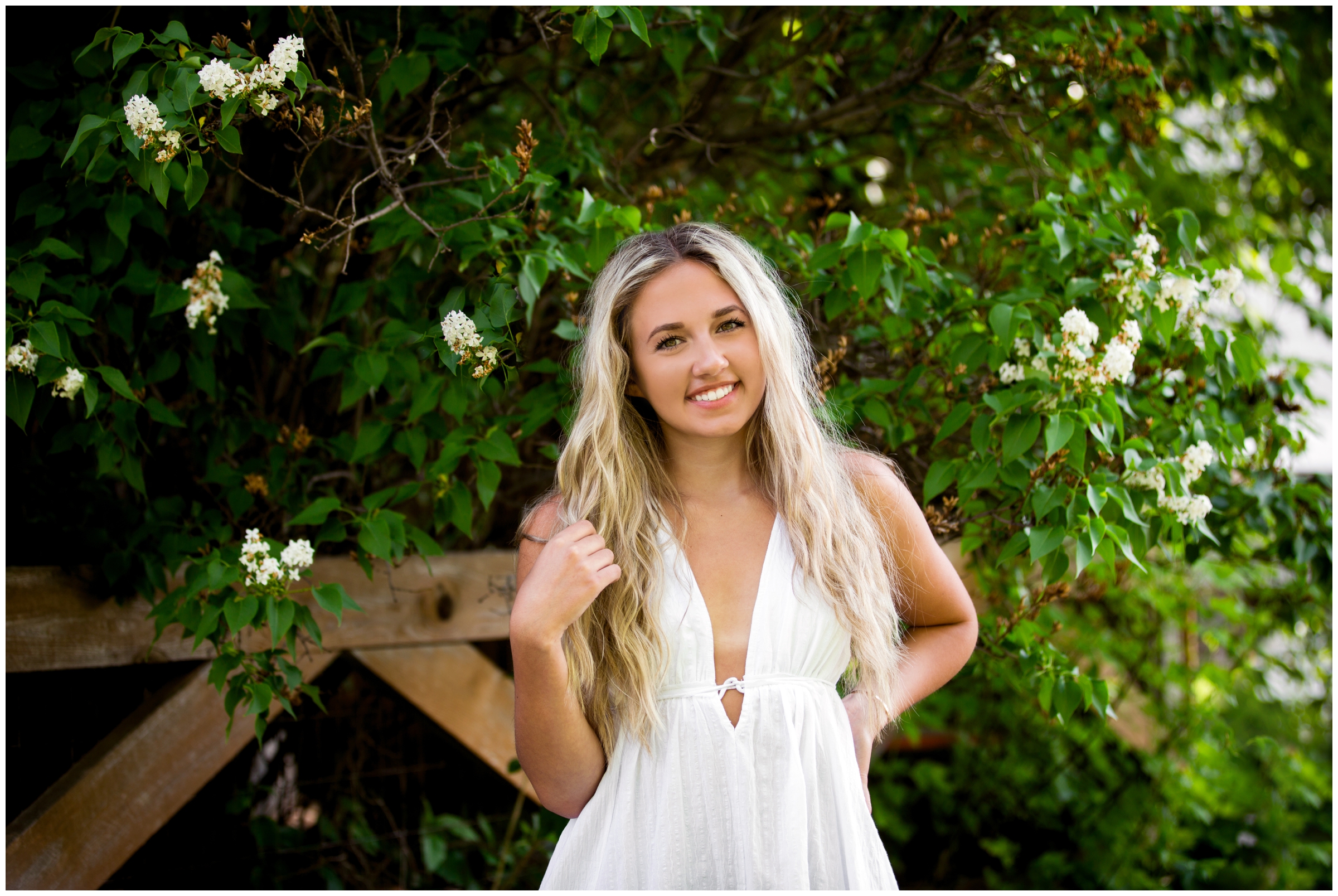 teen in white dress posing by lilac bush during summer Broomfield senior photos