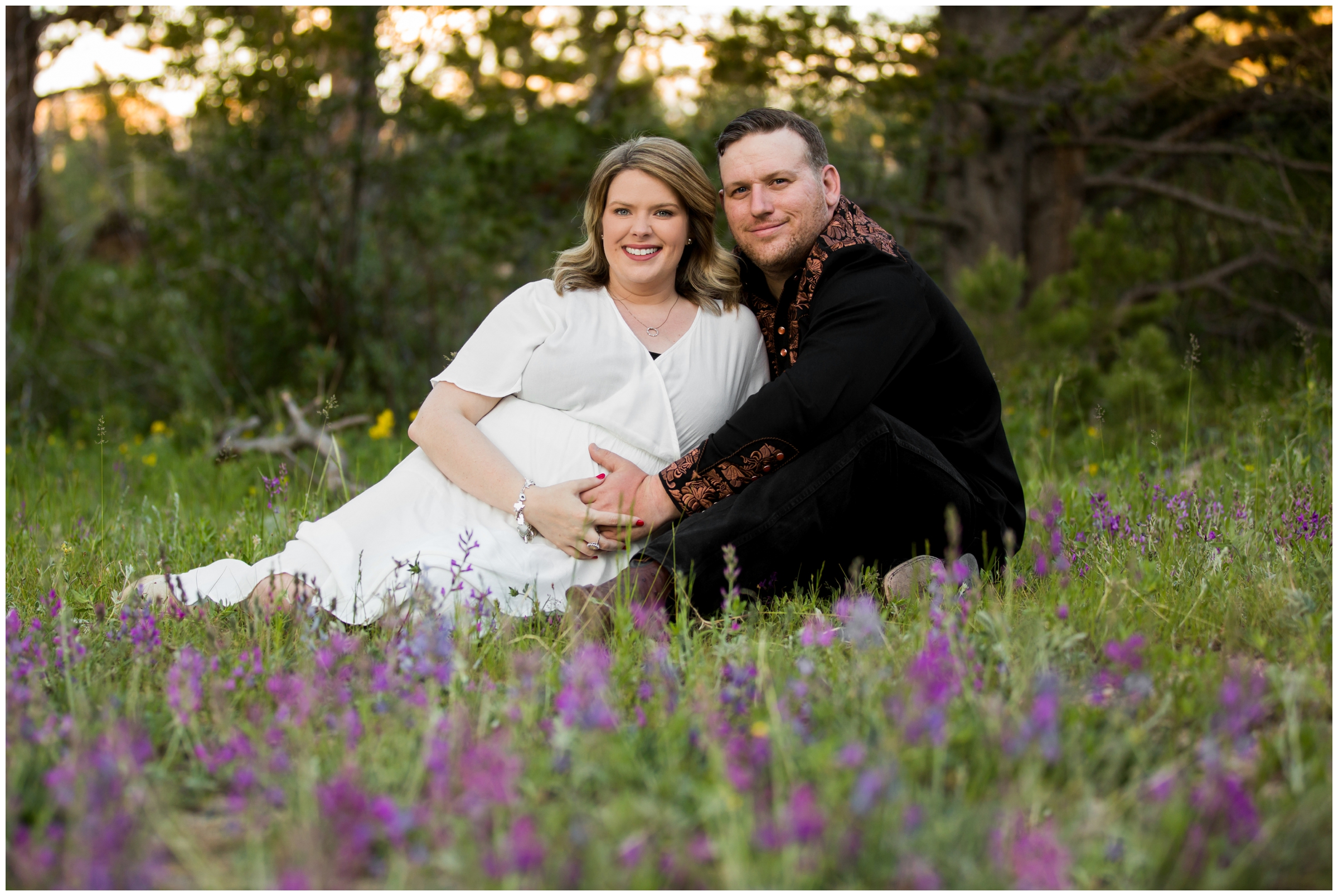 couple sitting in field of wildflowers during Estes Park maternity pictures in RMNP