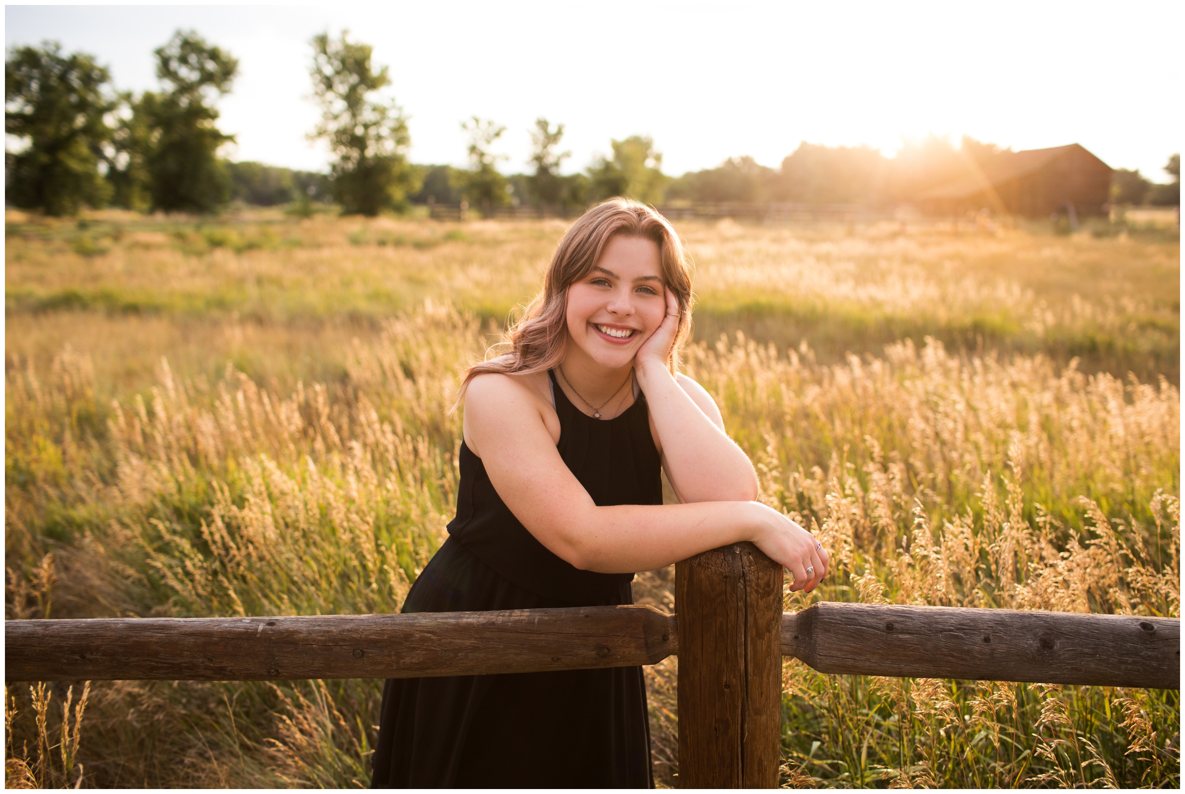 teen leaning on fence with barn in background during Sandstone Ranch senior pictures in Longmont Colorado