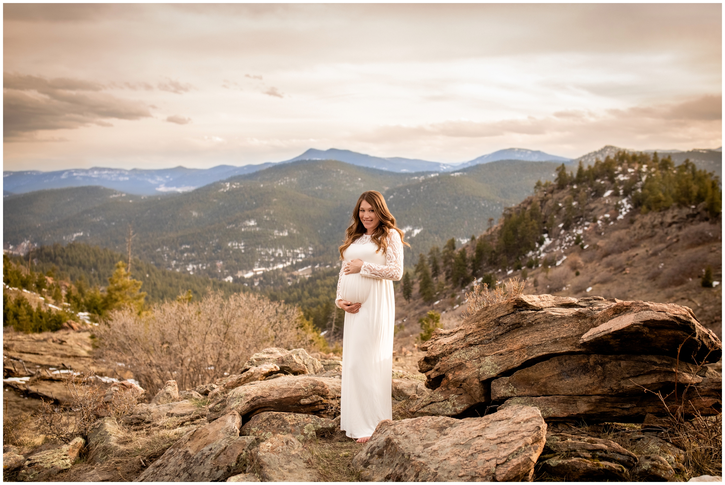 Woman in ivory dress holding belly during Colorado maternity photos at mount falcon west 