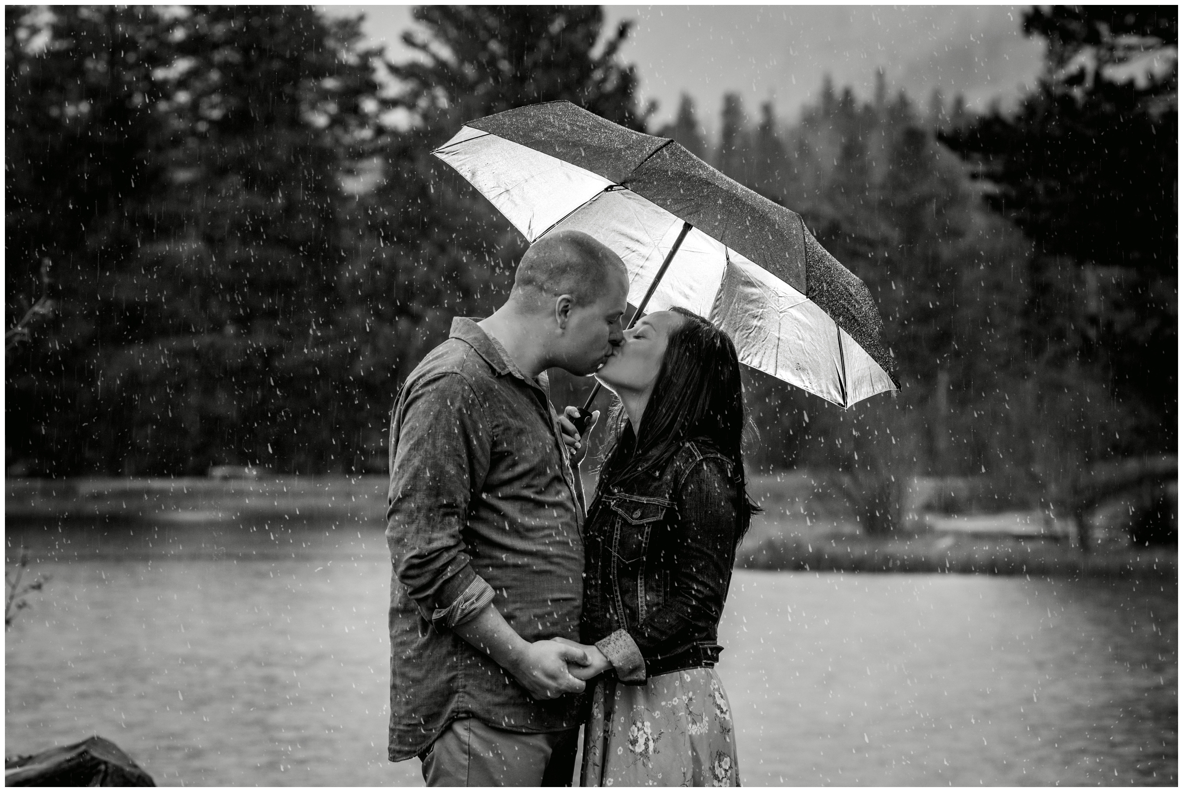couple kissing under an umbrella during estes park rainy engagement photos at Sprague Lake RMNP